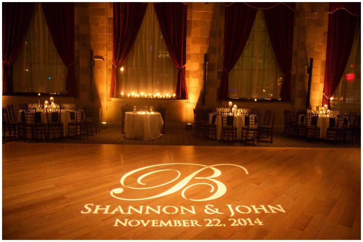 Elegant wedding reception hall with lit candles and dance floor monogram reading “Shannon & John, November 22, 2014”