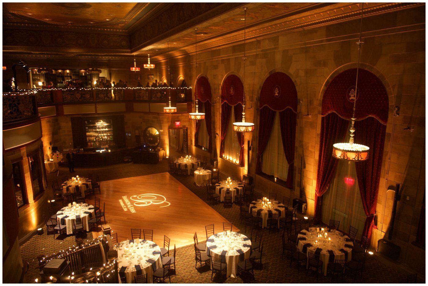 Elegant banquet hall with round tables, warm amber lighting, and a balcony overlooking the dining floor