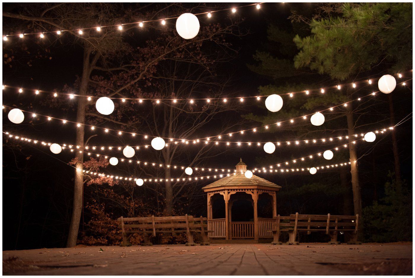String lights hang over a wooden gazebo in a dark outdoor park at night.