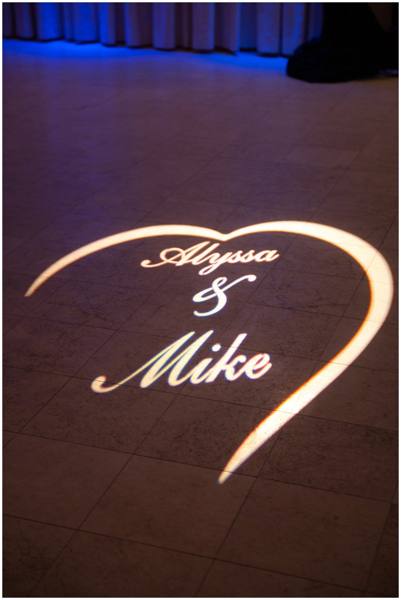 Projected white script names “Alyssa & Mike” on a dimly lit floor.
