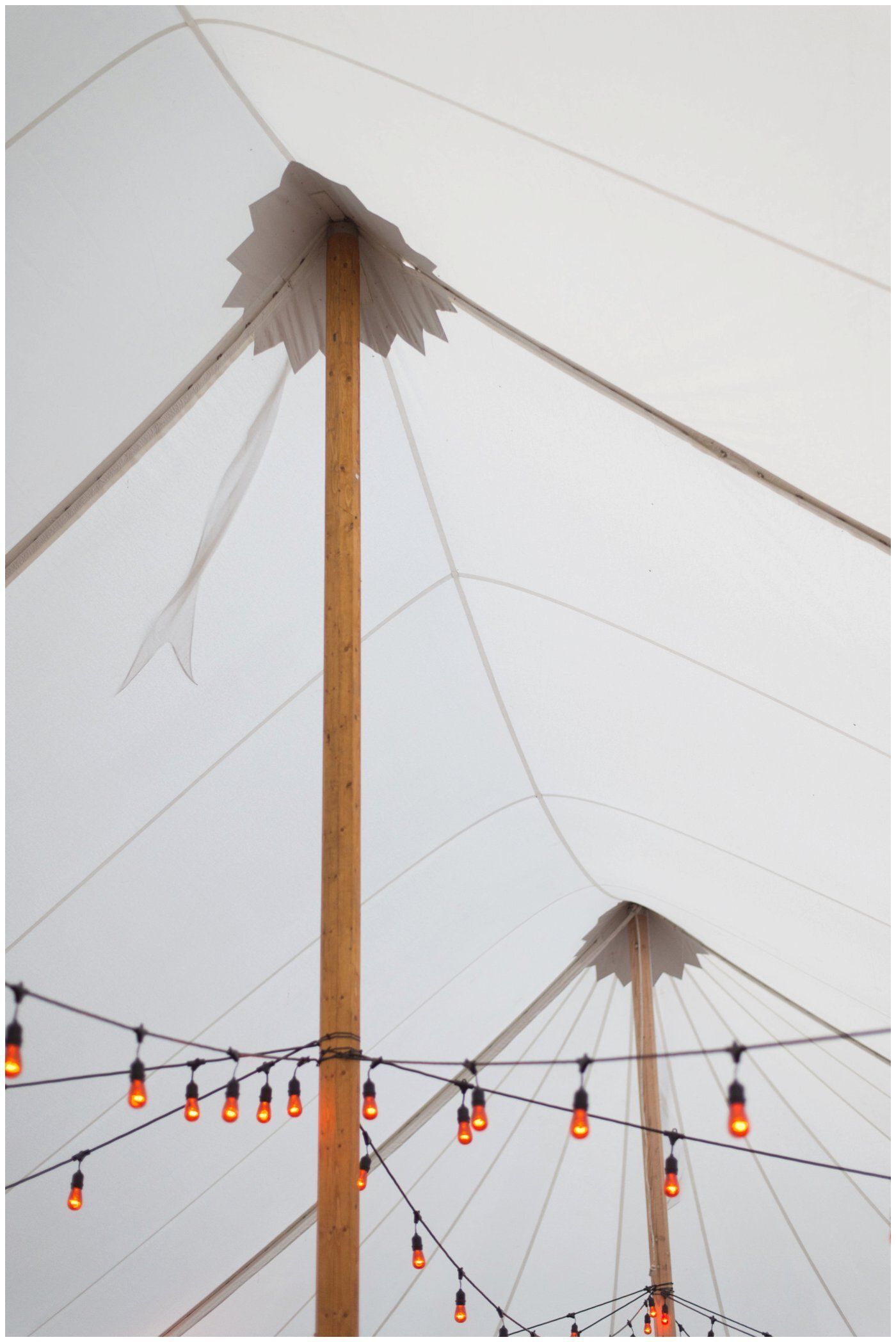 Tall wooden pole in a white tent with string lights and cables overhead