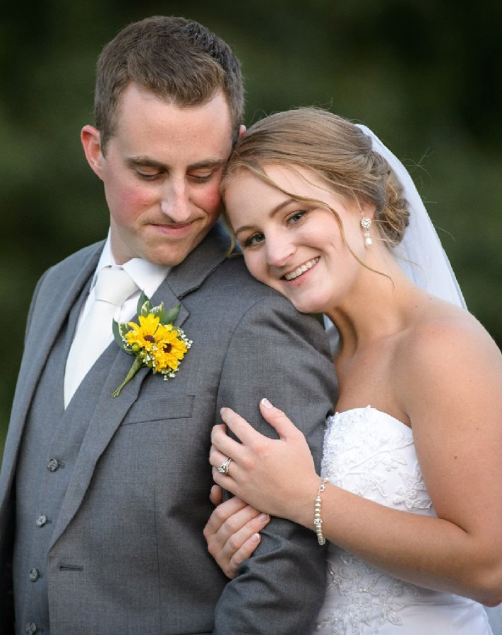 Bride and groom embracing, smiling in wedding attire, with a yellow boutonniere