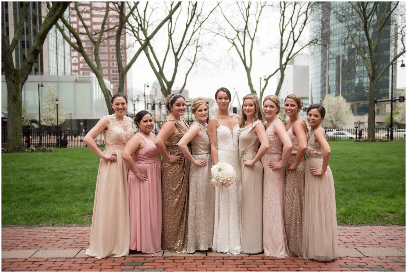 Bridesmaids and bride posing outdoors in blush and gold dresses in a park-like city setting