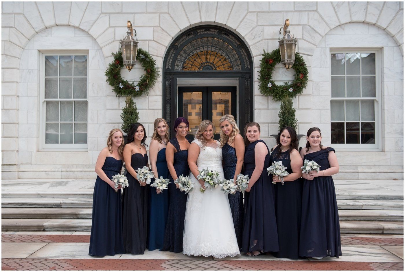 Bridal party posing on church steps, bride in white gown with attendants in navy dresses holding bouquets