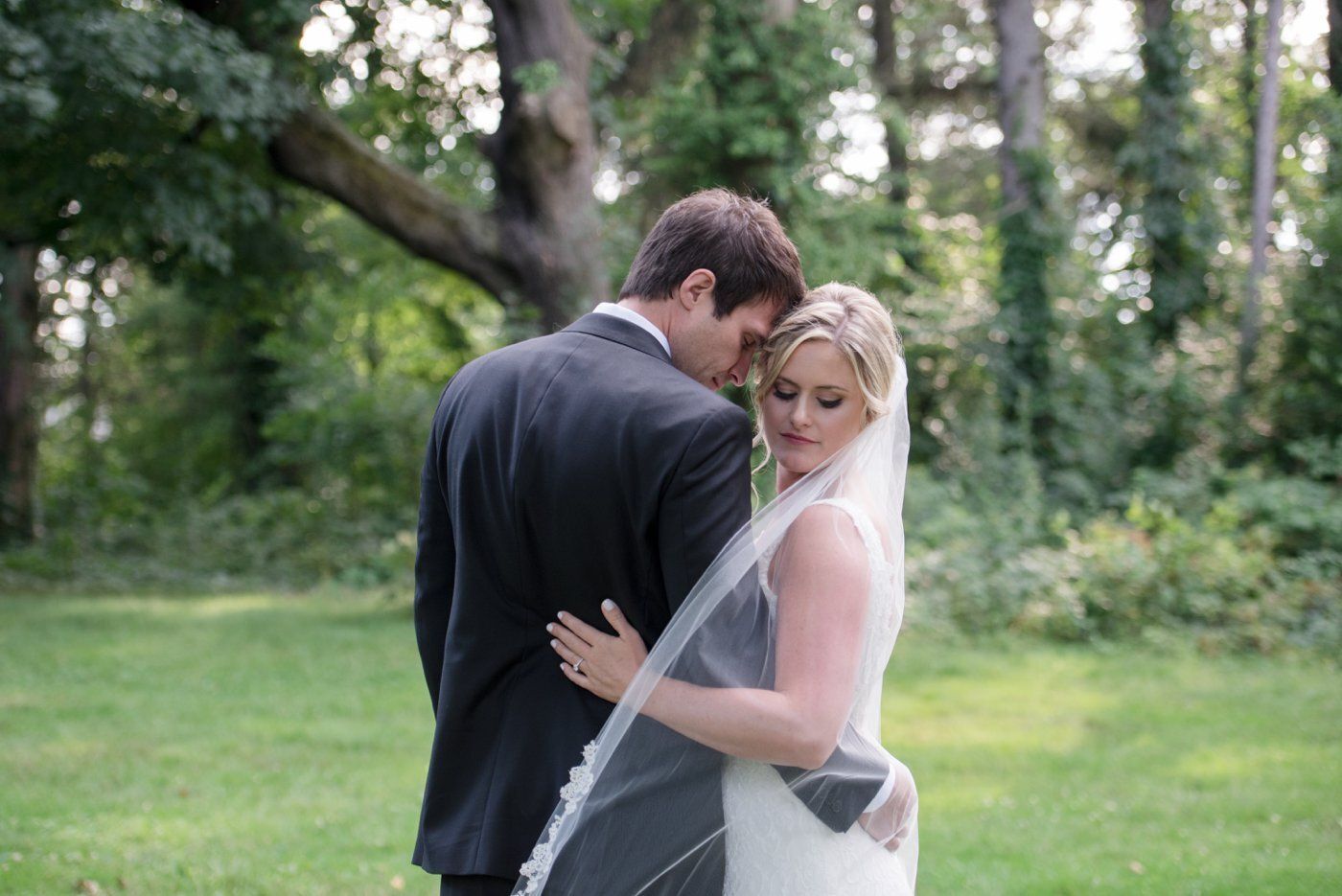 Bride and groom embracing outdoors in a green garden, bride in veil and gown