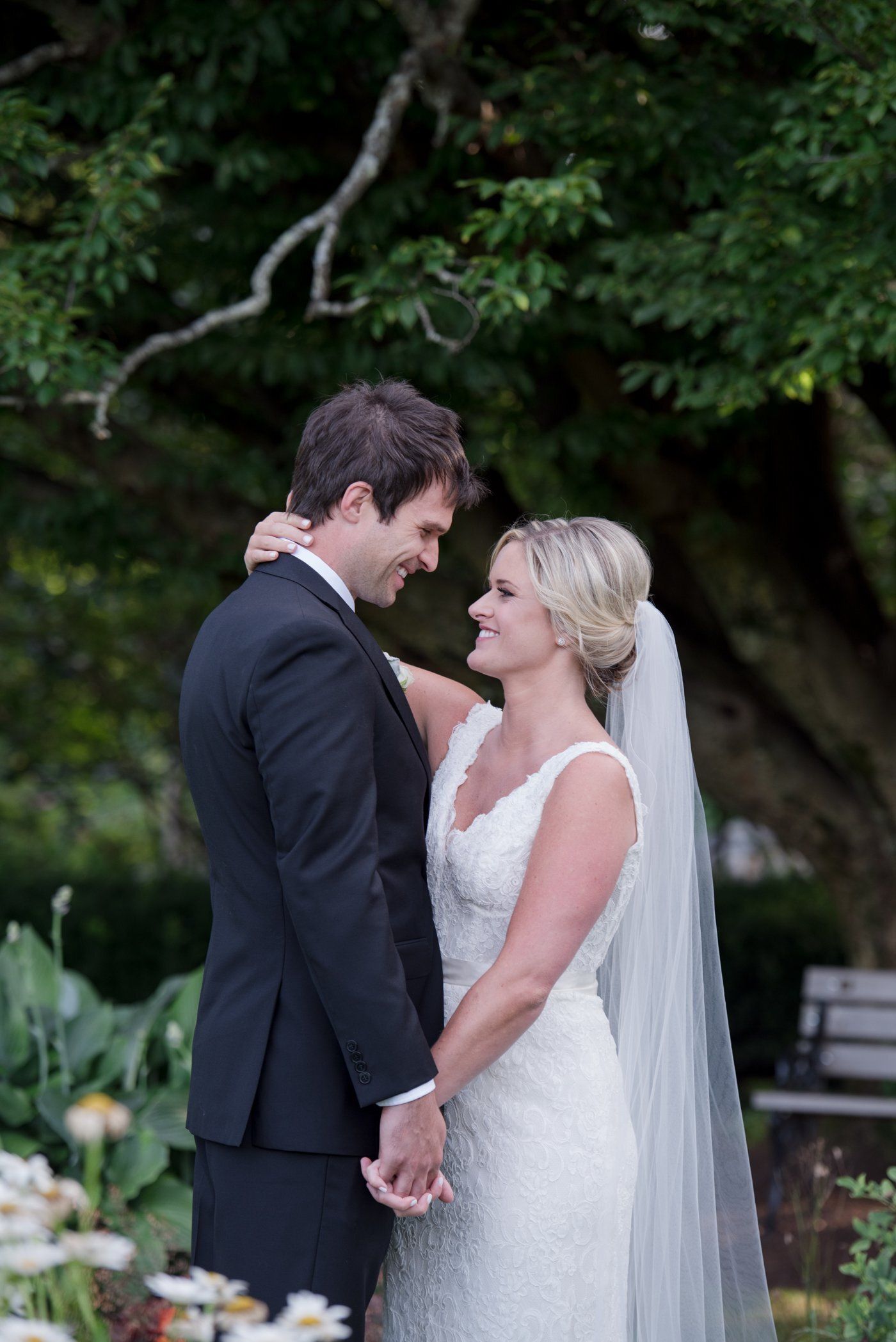 Bride and groom holding hands outdoors, facing each other in a garden wedding setting.
