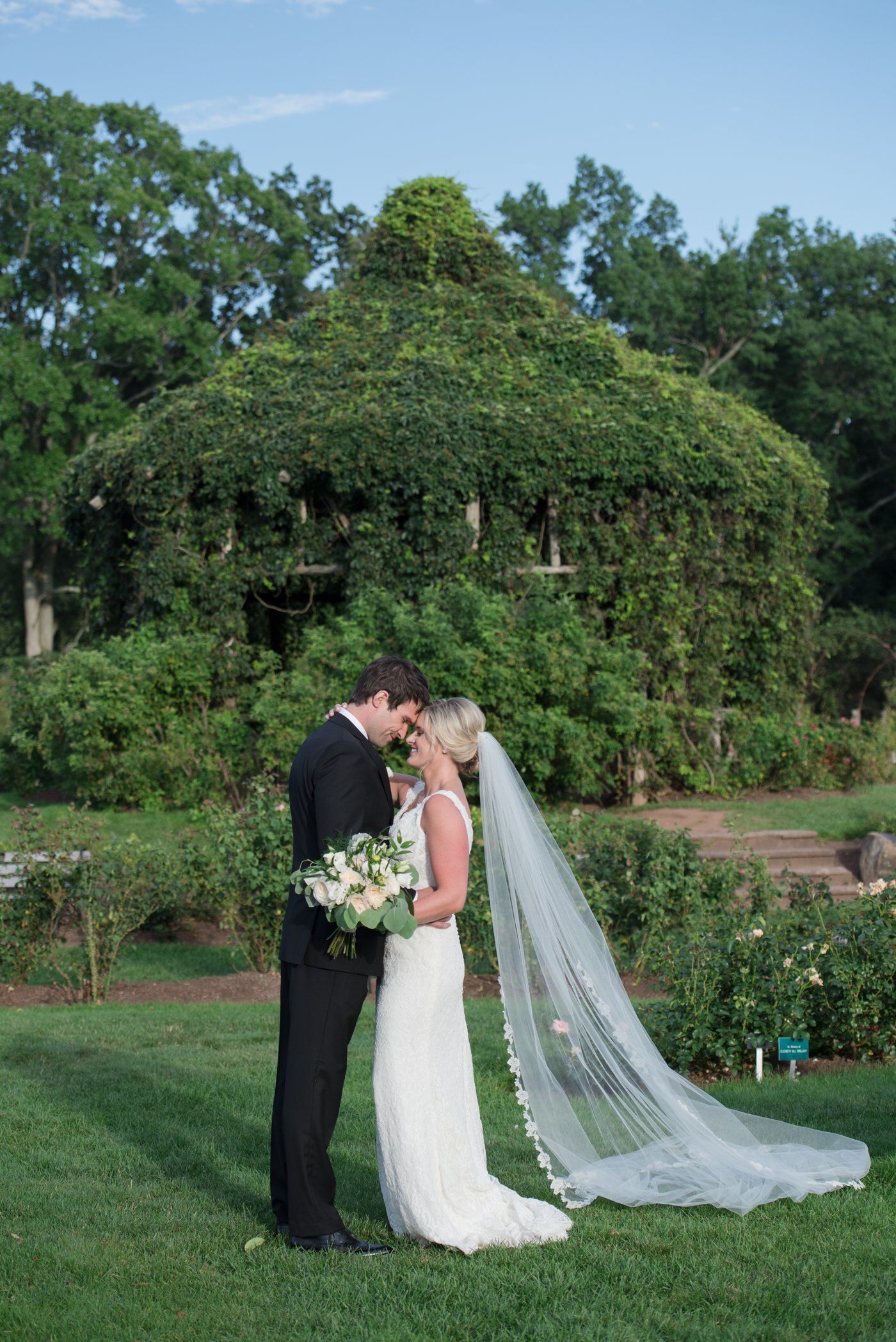 Bride and groom kissing in a garden, with a long veil trailing on the grass