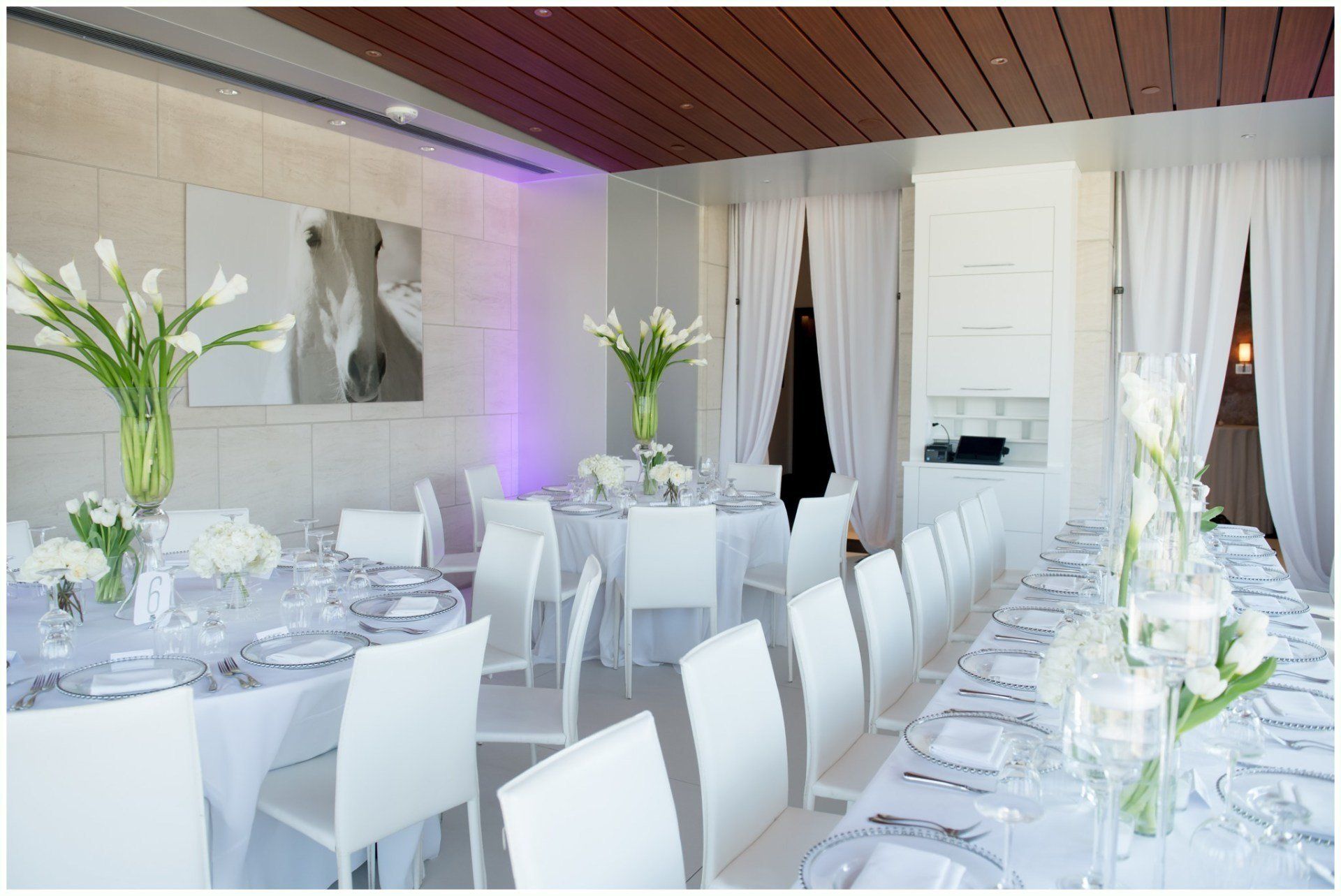 Elegant white banquet room with long set tables, floral centerpieces, and soft purple accent lighting