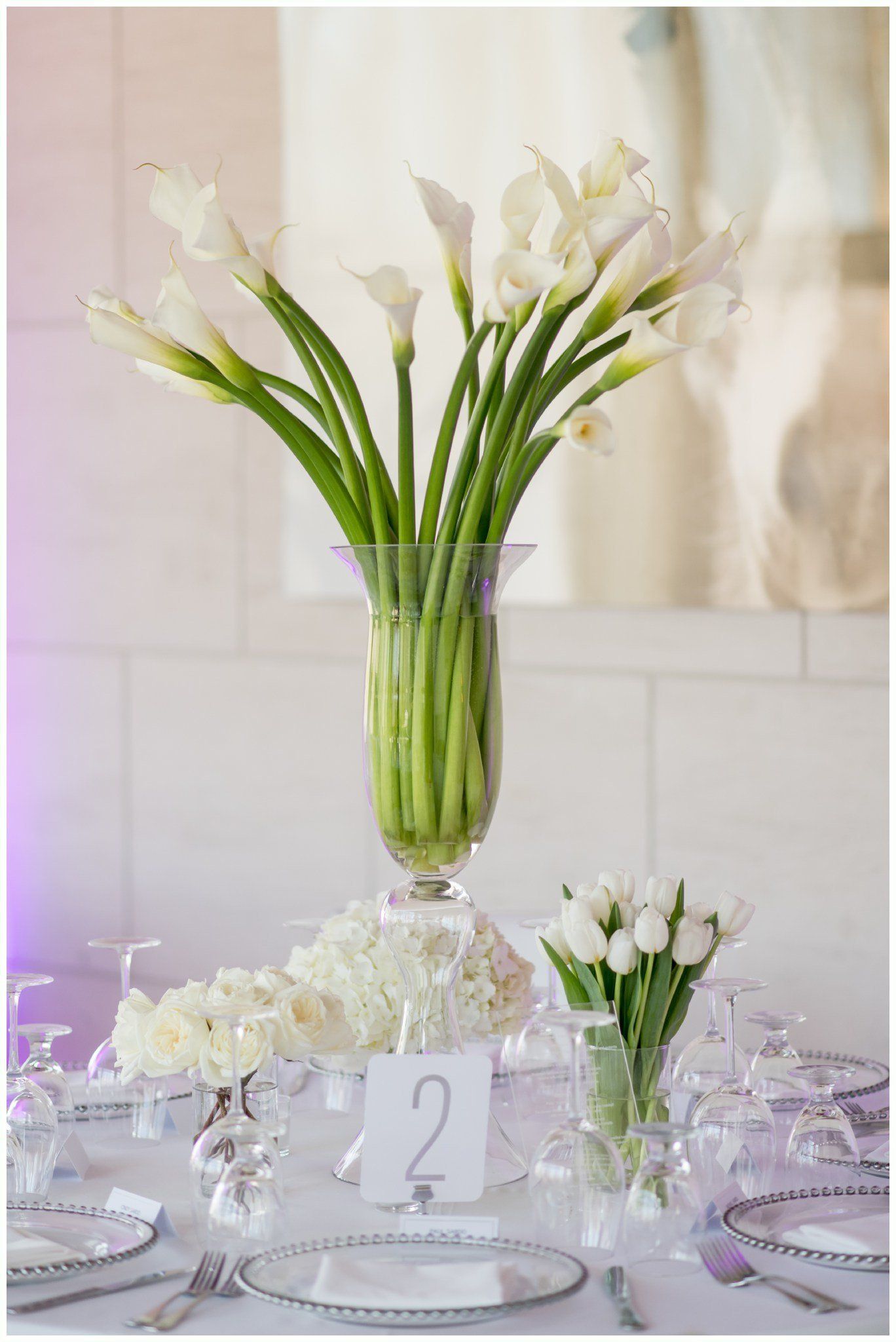 Elegant white floral centerpiece in a glass vase on a decorated table with candles and place cards