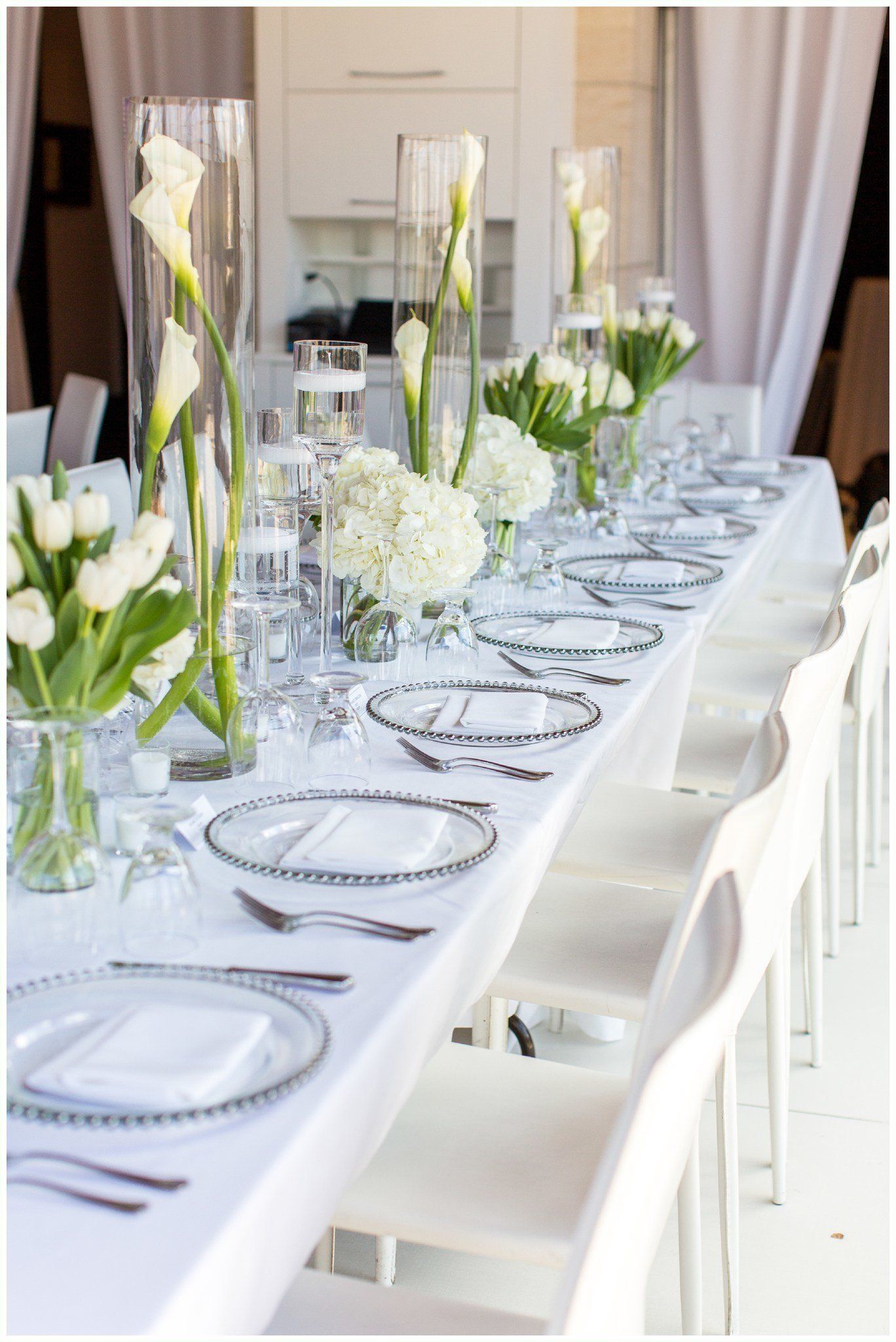 Elegant banquet table set with white chairs, glassware, and green-and-white floral centerpieces