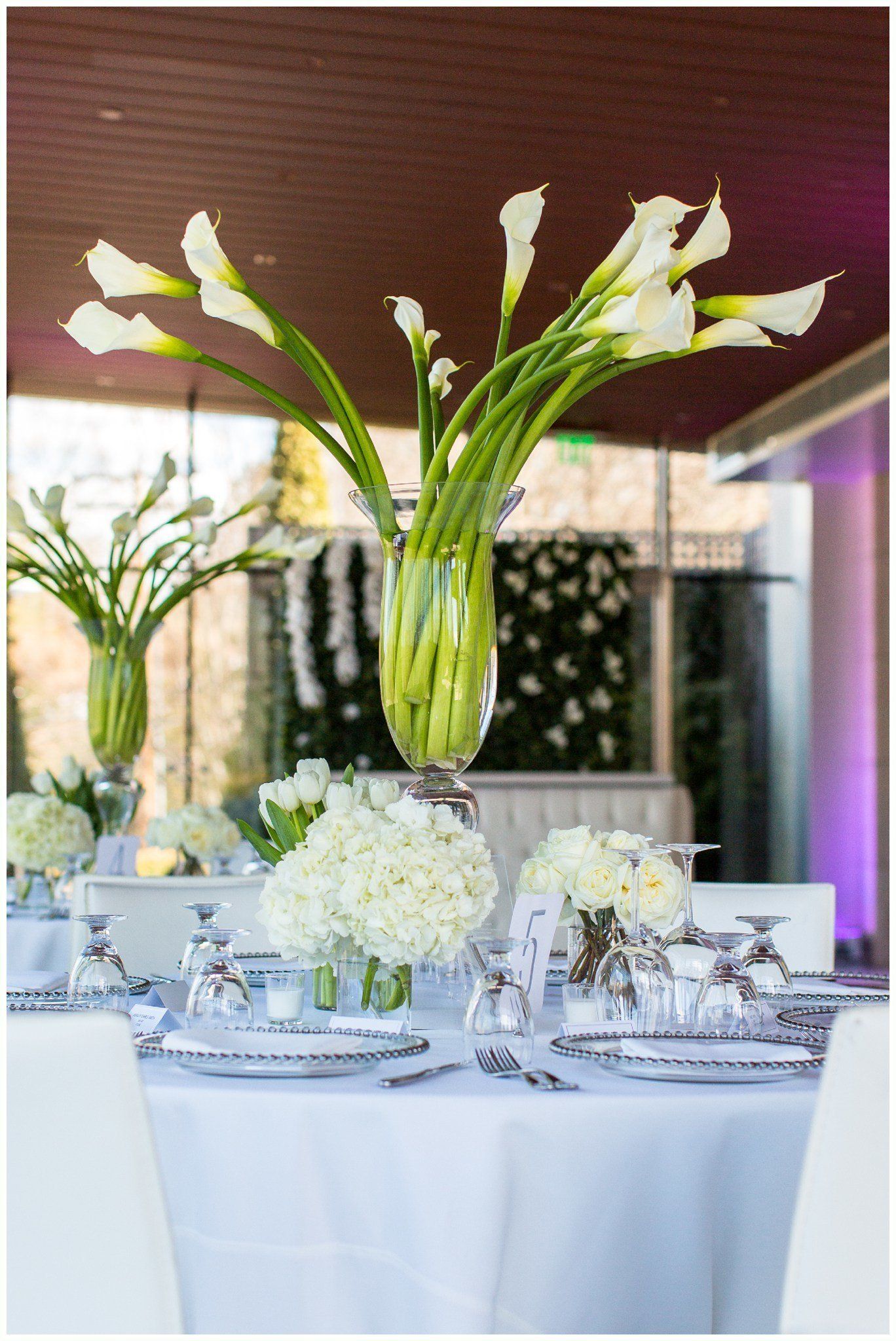 Elegant wedding reception table with white floral centerpieces and tall calla lily arrangement