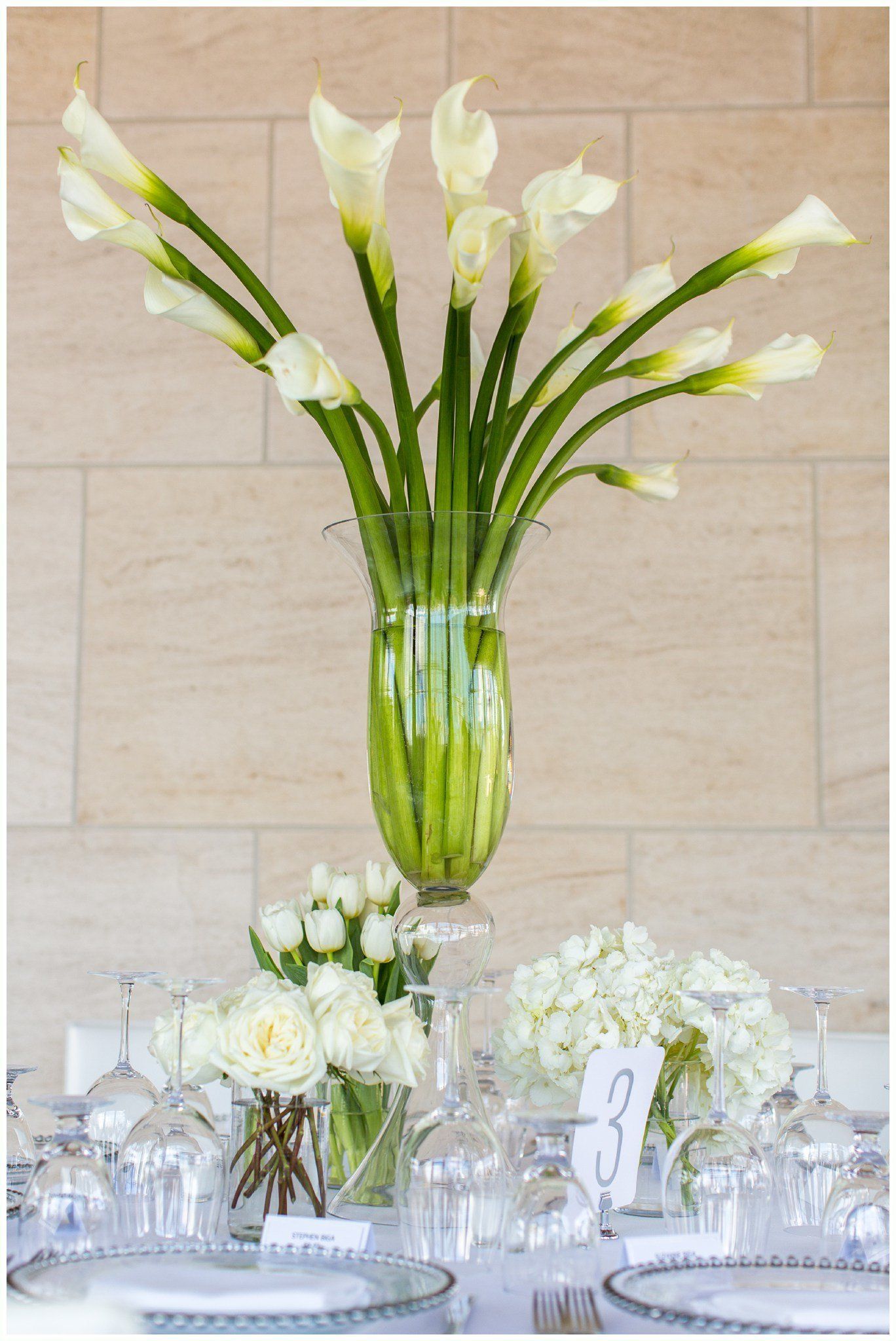 Elegant banquet table centerpiece with tall white calla lilies in a clear glass vase