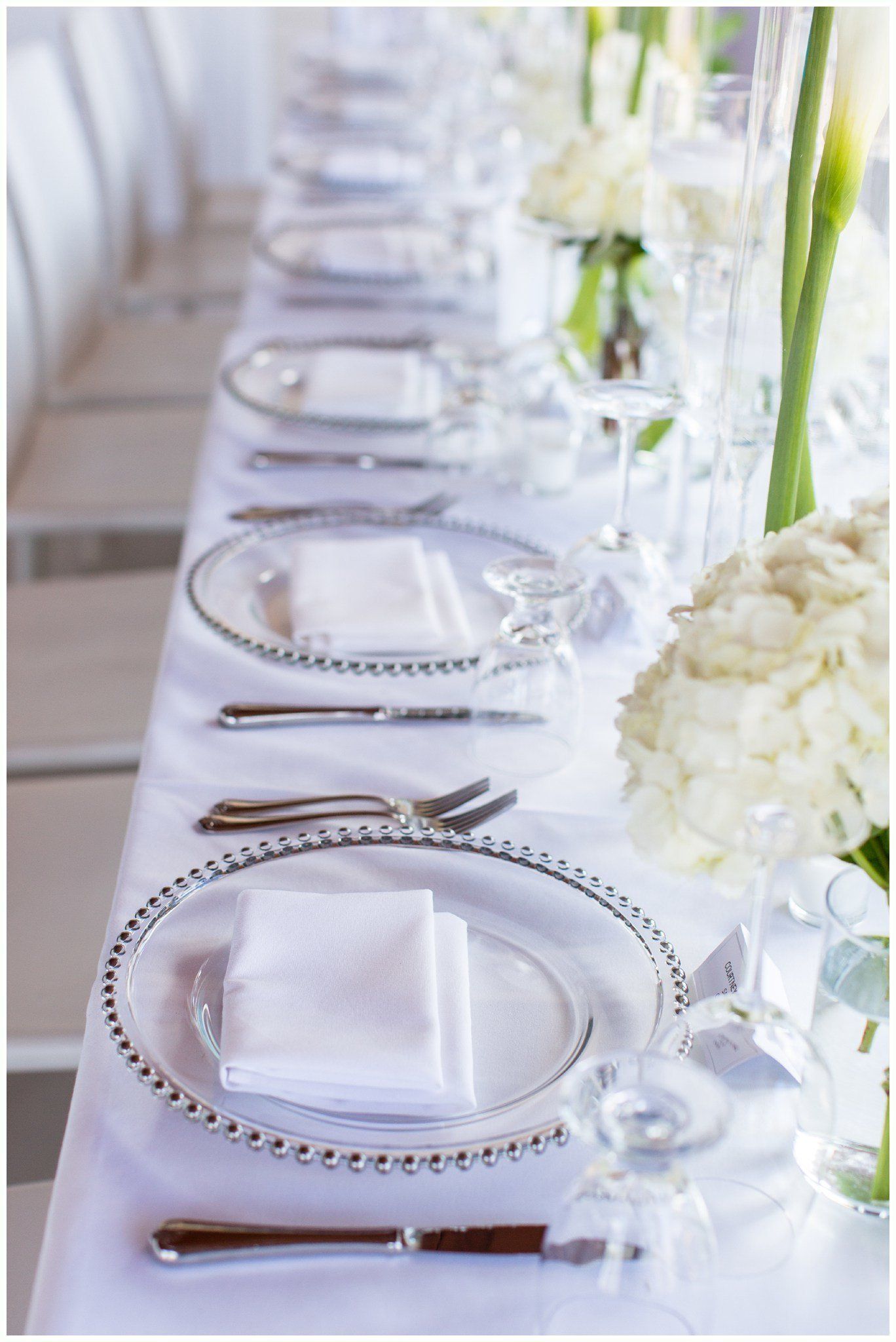Elegant white table setting with silver chargers, folded napkins, and floral centerpieces for a formal event