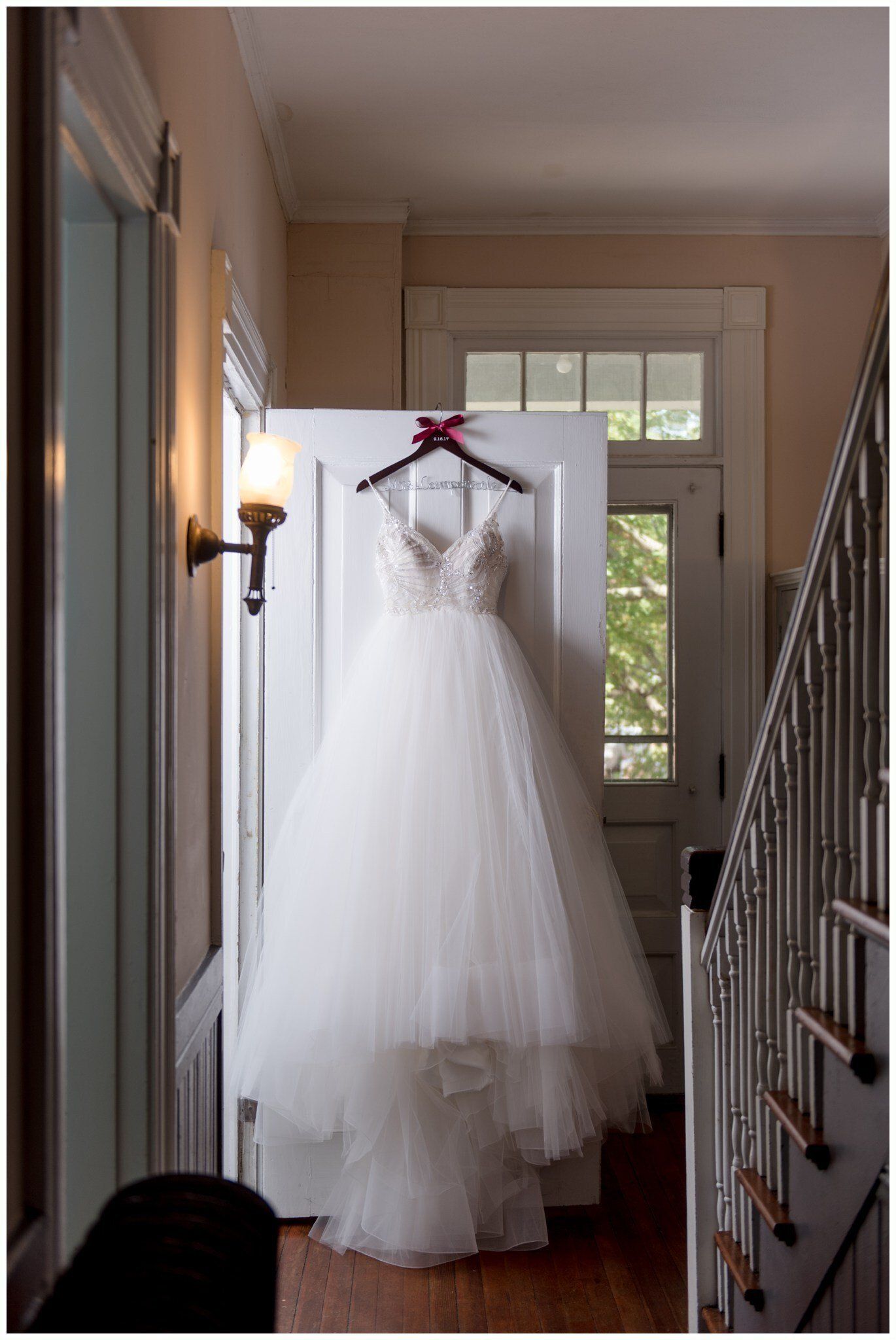 Wedding dress hanging in a hallway, backlit by a doorway and window