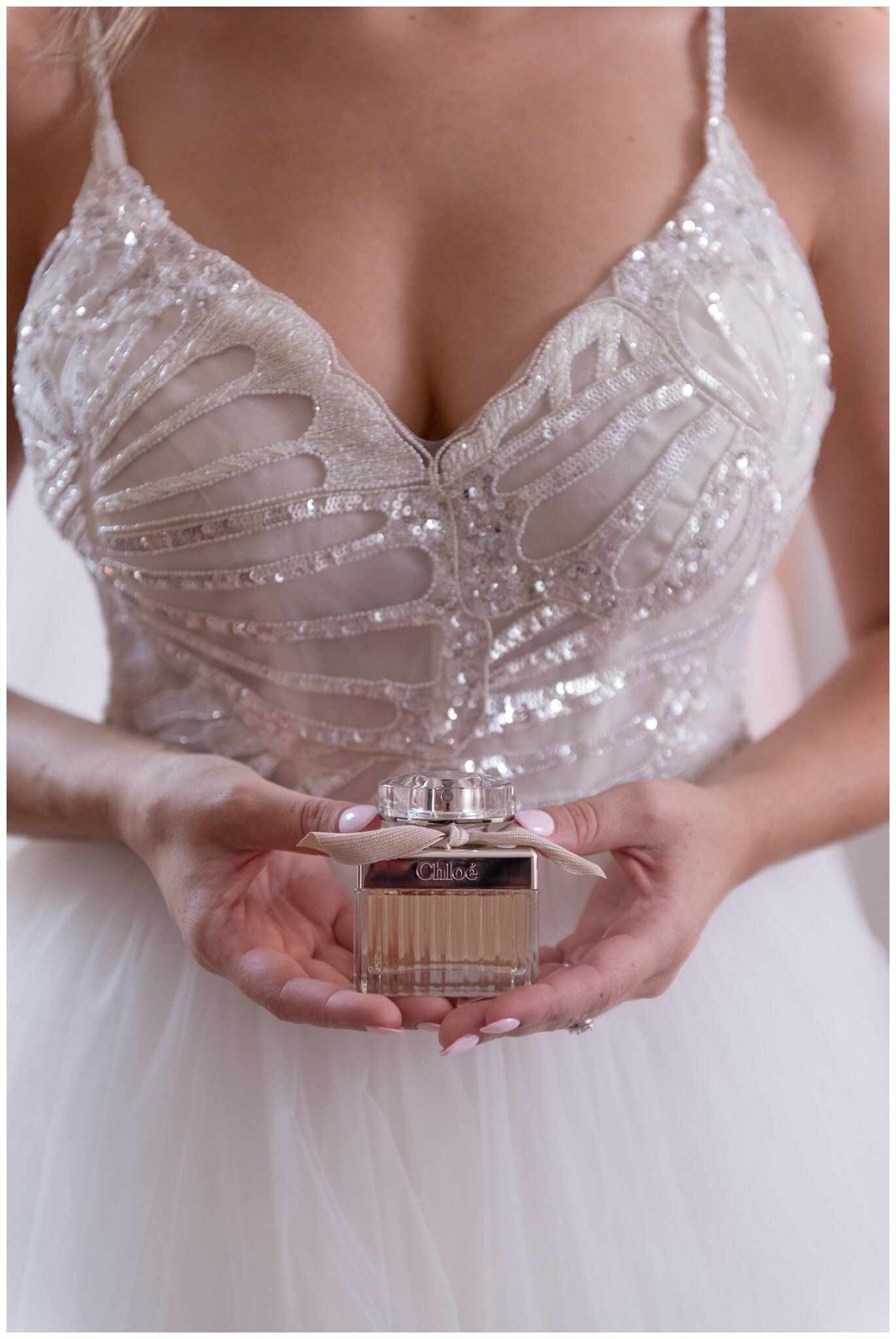Woman in a white beaded dress holding a small perfume bottle in both hands