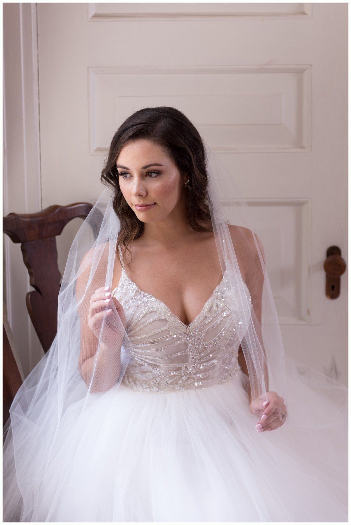 Bride in a white wedding dress and veil standing by a door, holding her gown
