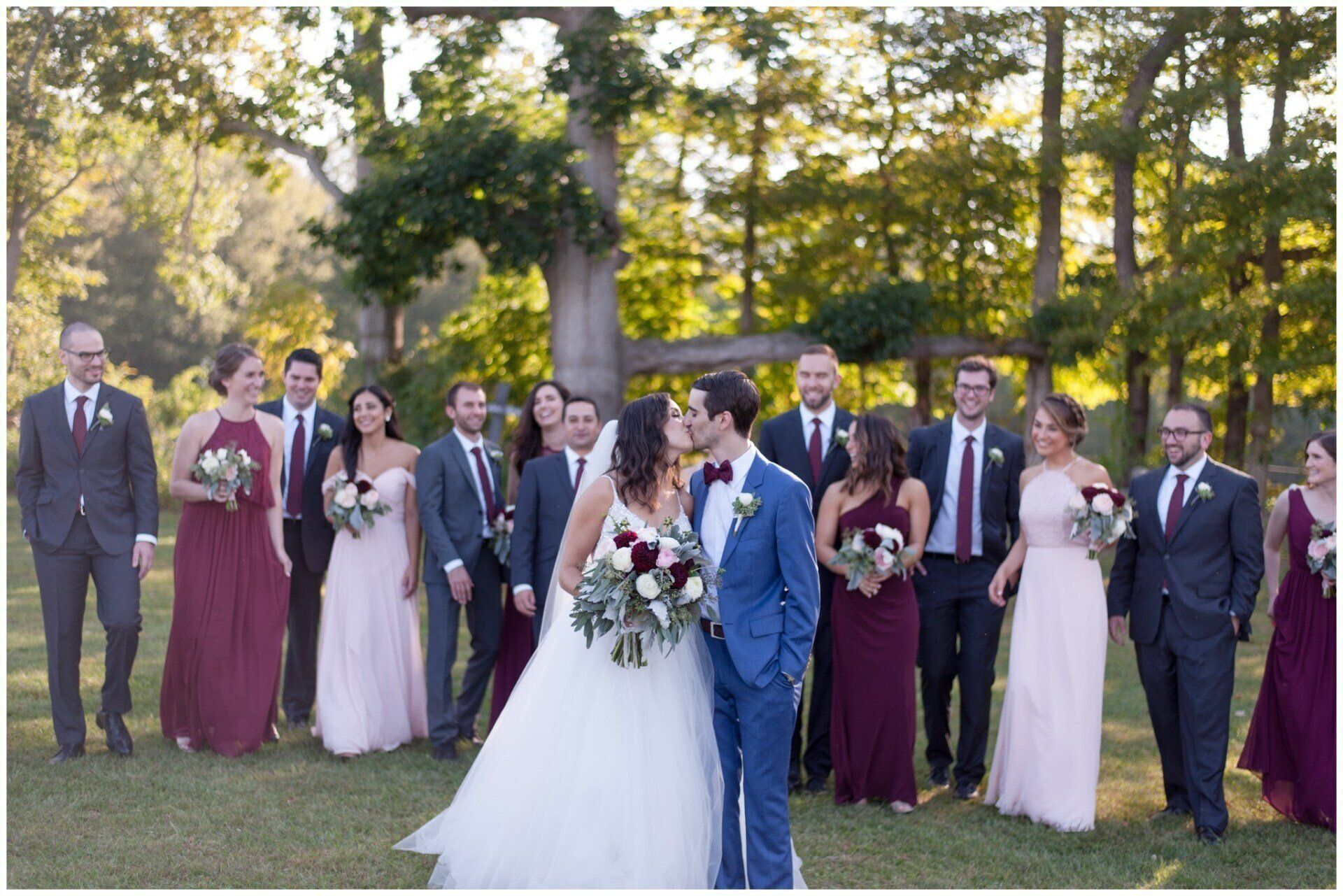 Wedding party posing outdoors in formal attire, with the bride and groom centered in front