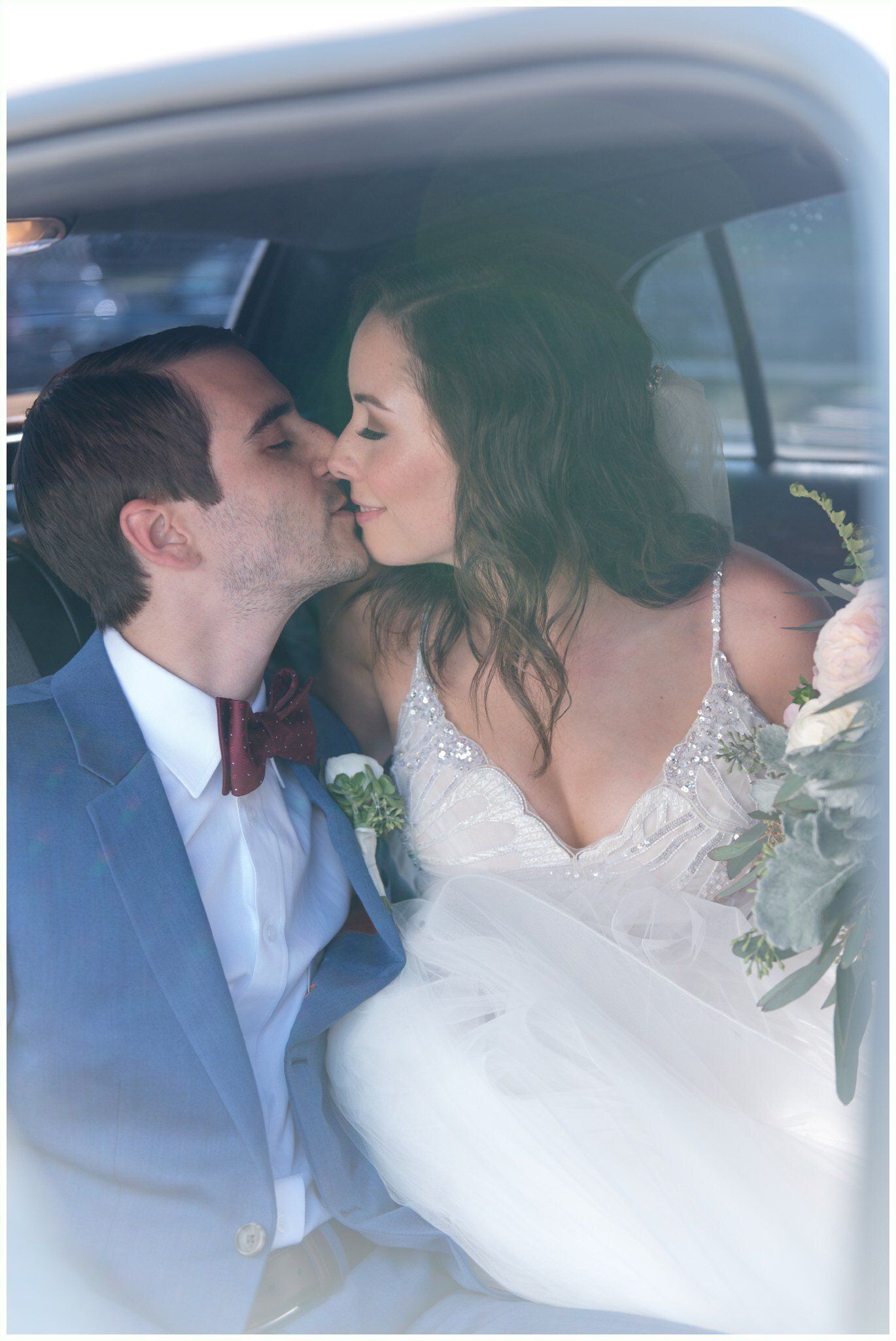 Couple kissing in a car, with the bride in a white dress and bouquet visible.