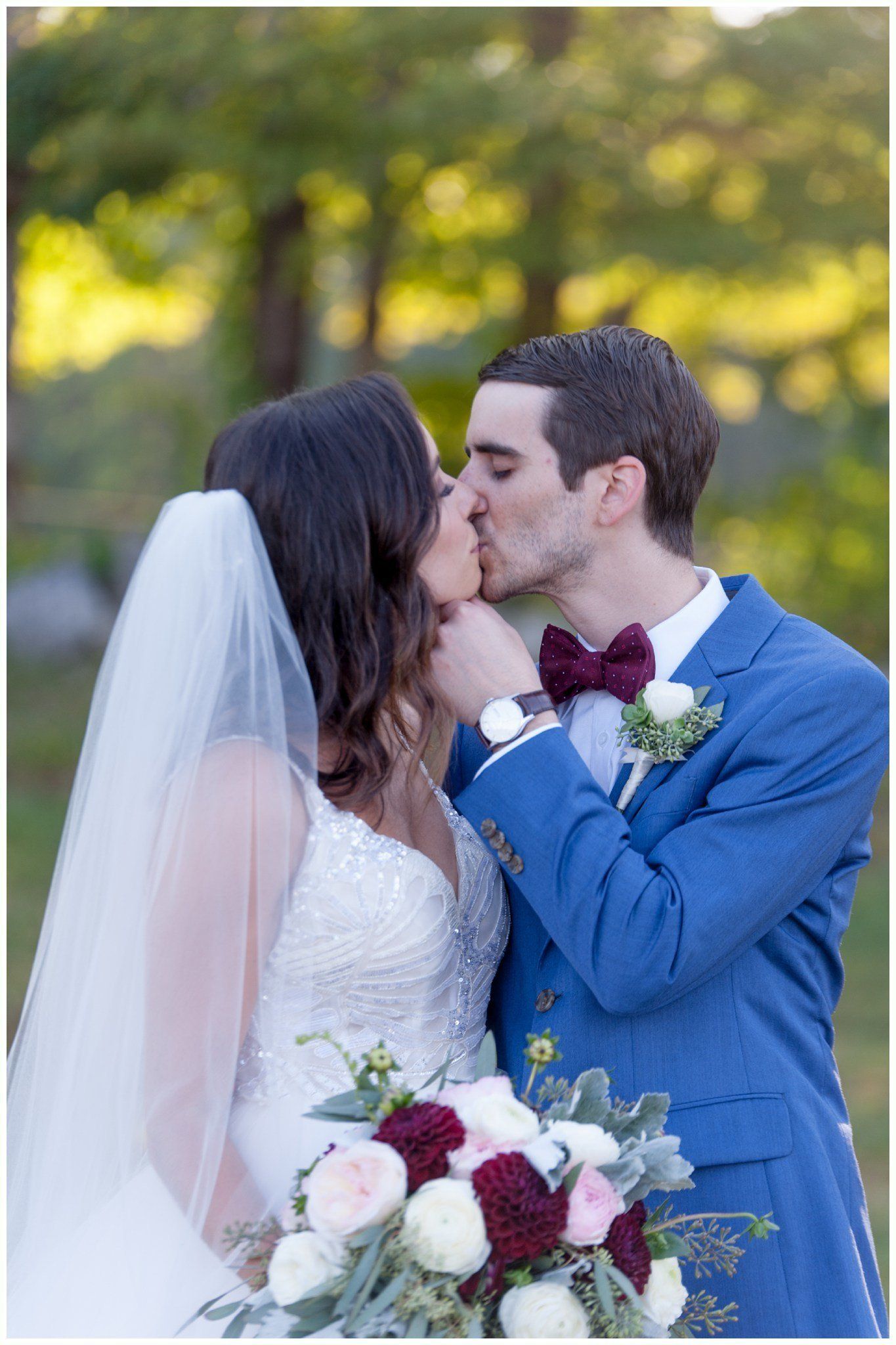 Bride and groom kissing outdoors, with bouquet and blue suit, against a soft green background