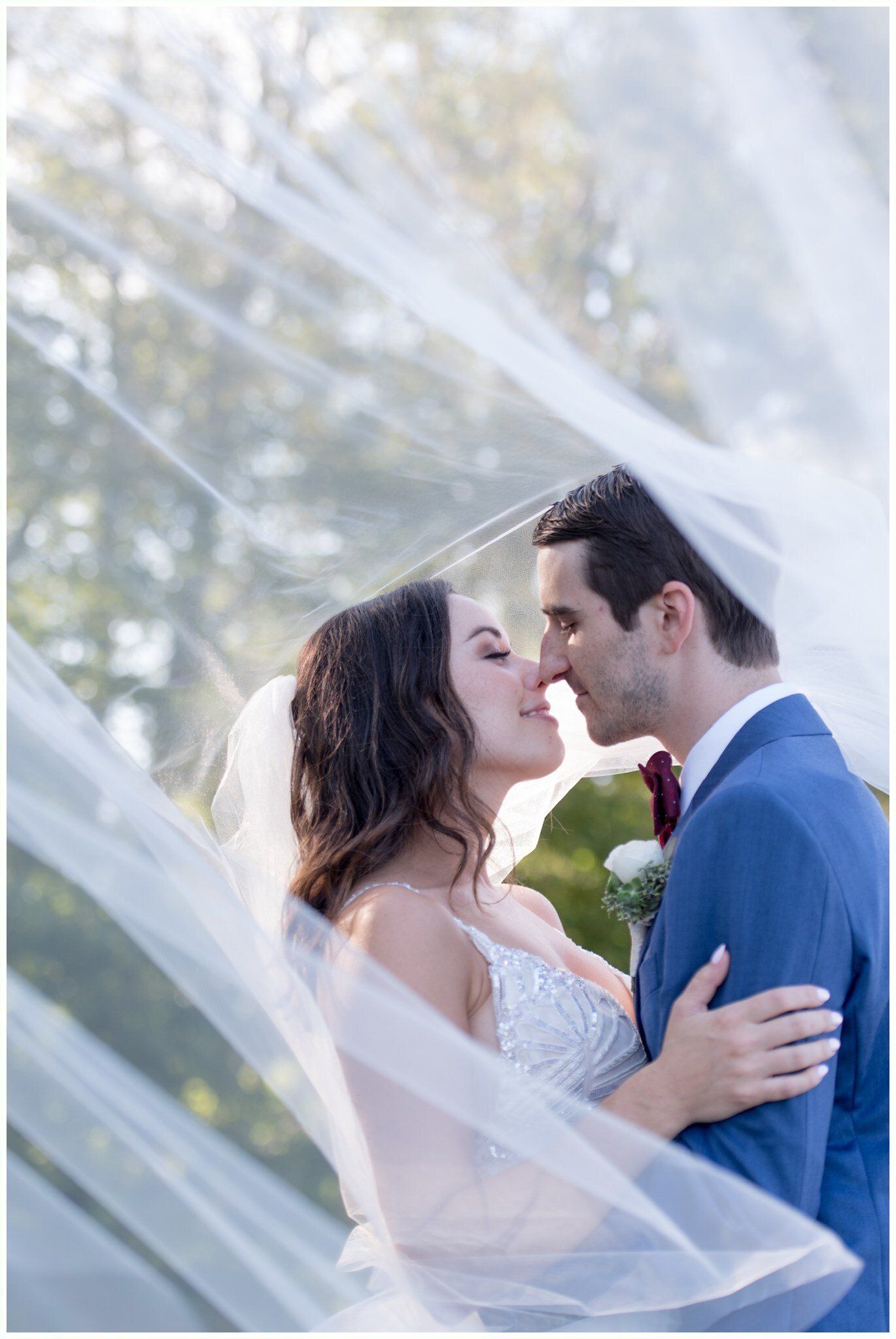 Bride and groom kissing under flowing white veil outdoors