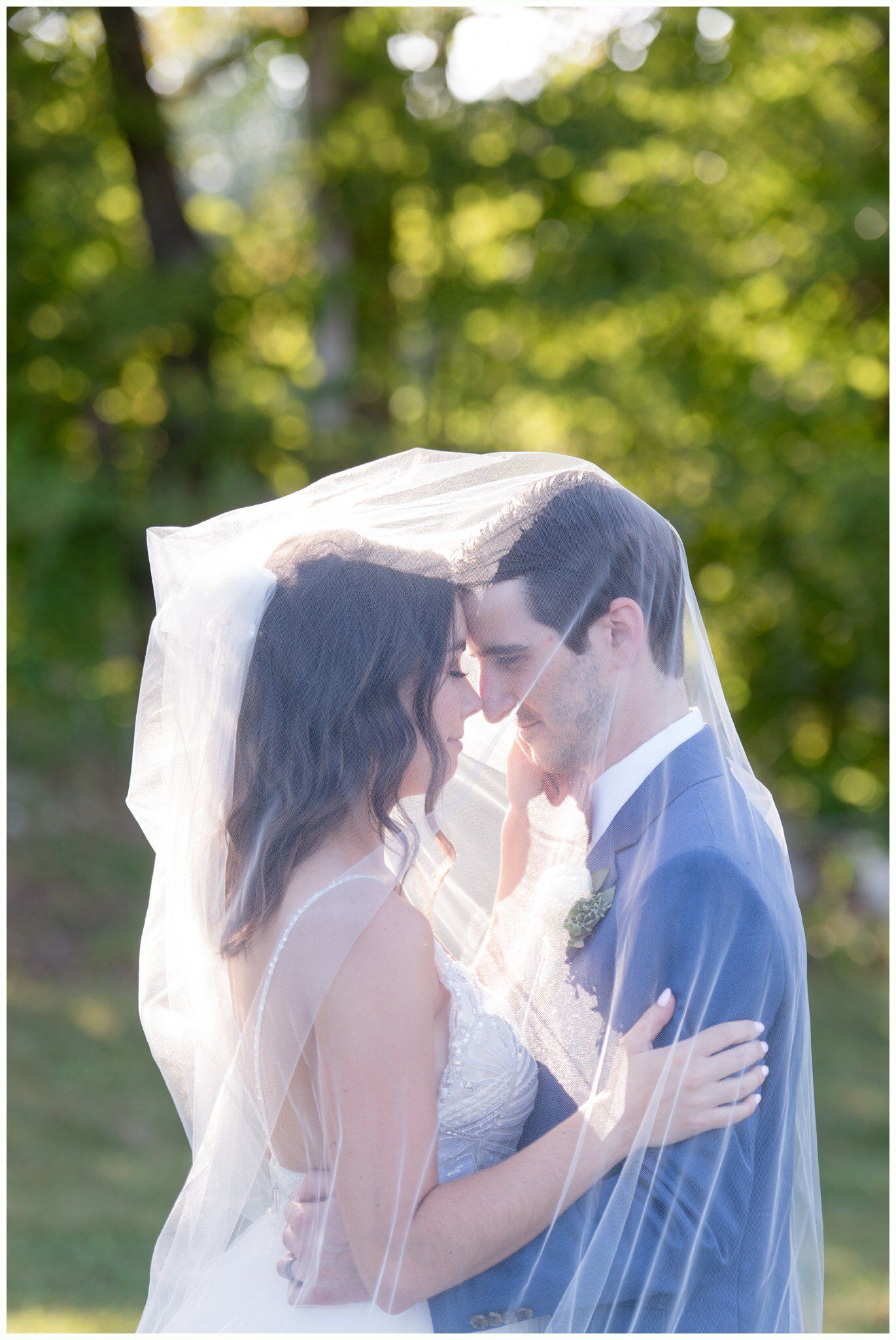 Bride and groom kissing under a veil in a sunlit outdoor setting