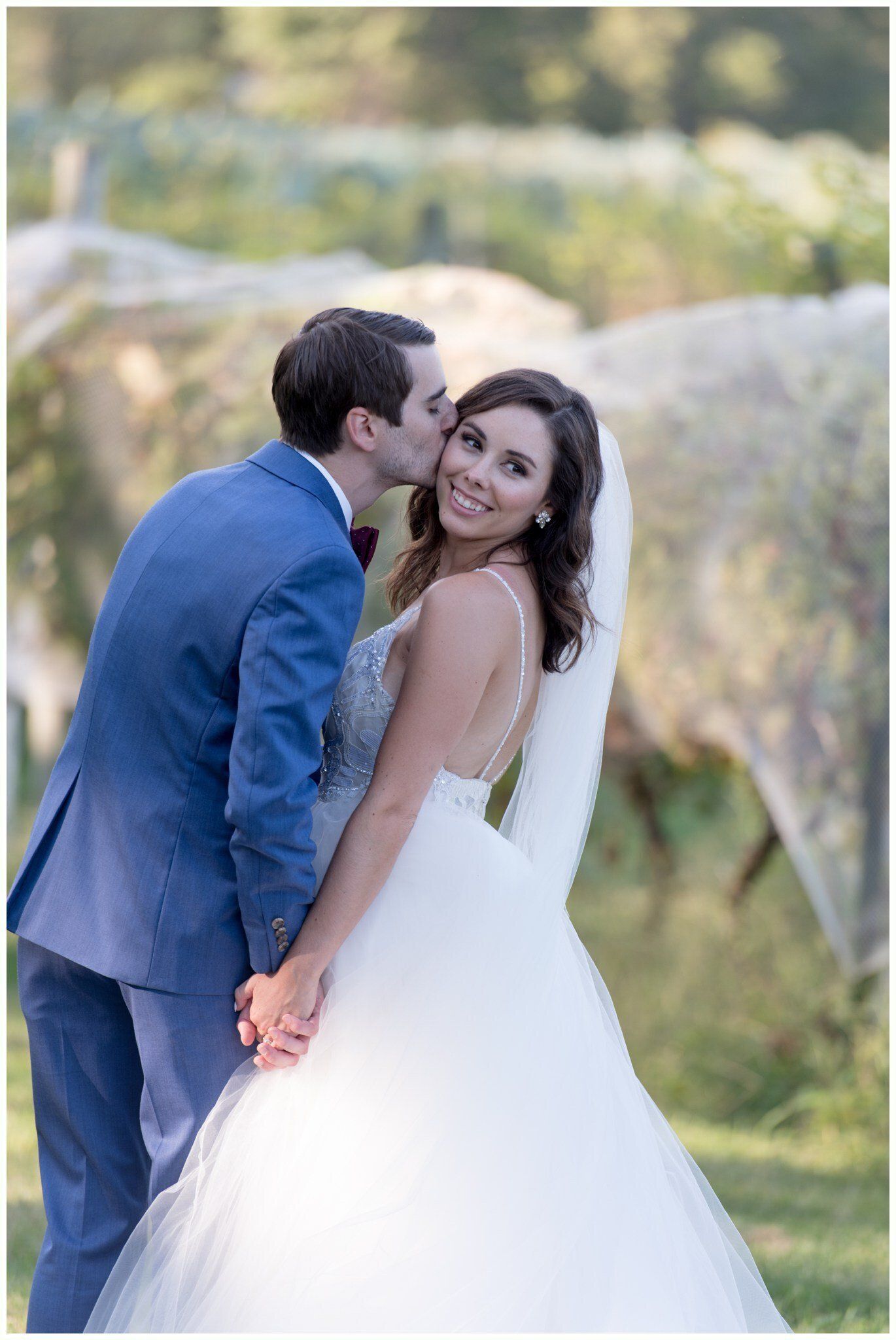 Bride and groom smiling outdoors, holding hands in a sunlit garden.