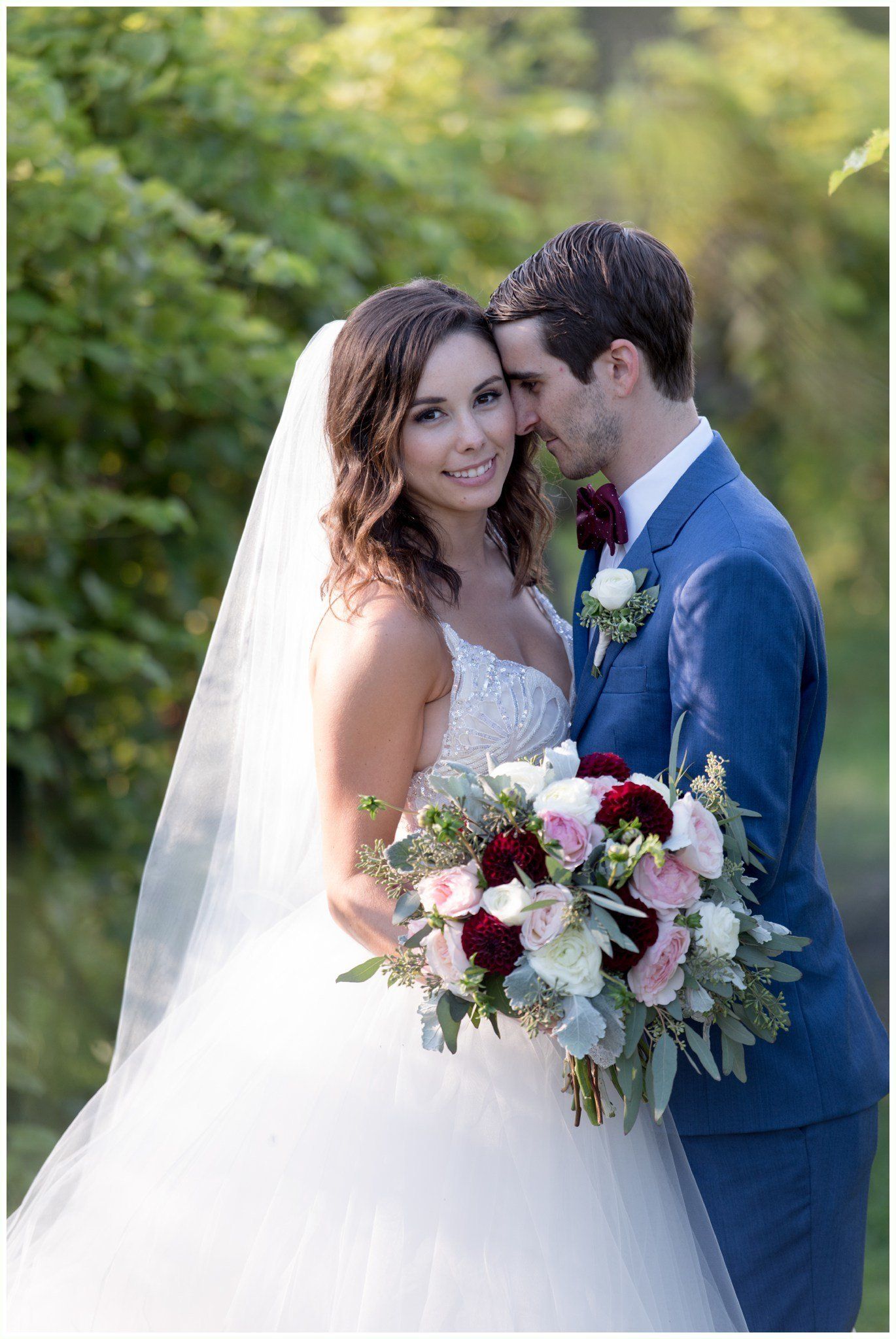 Bride and groom embracing outdoors, holding a bouquet in a sunlit garden
