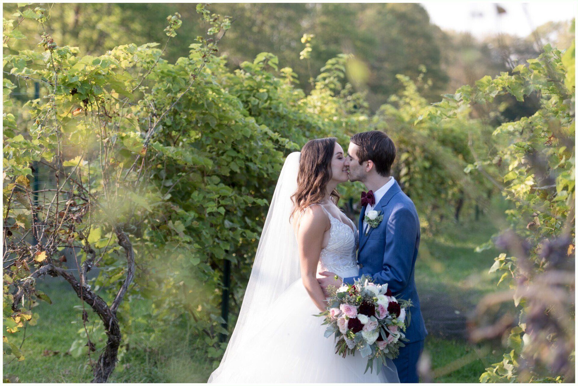 Bride and groom kiss in a sunlit garden, with the bride holding a bouquet.