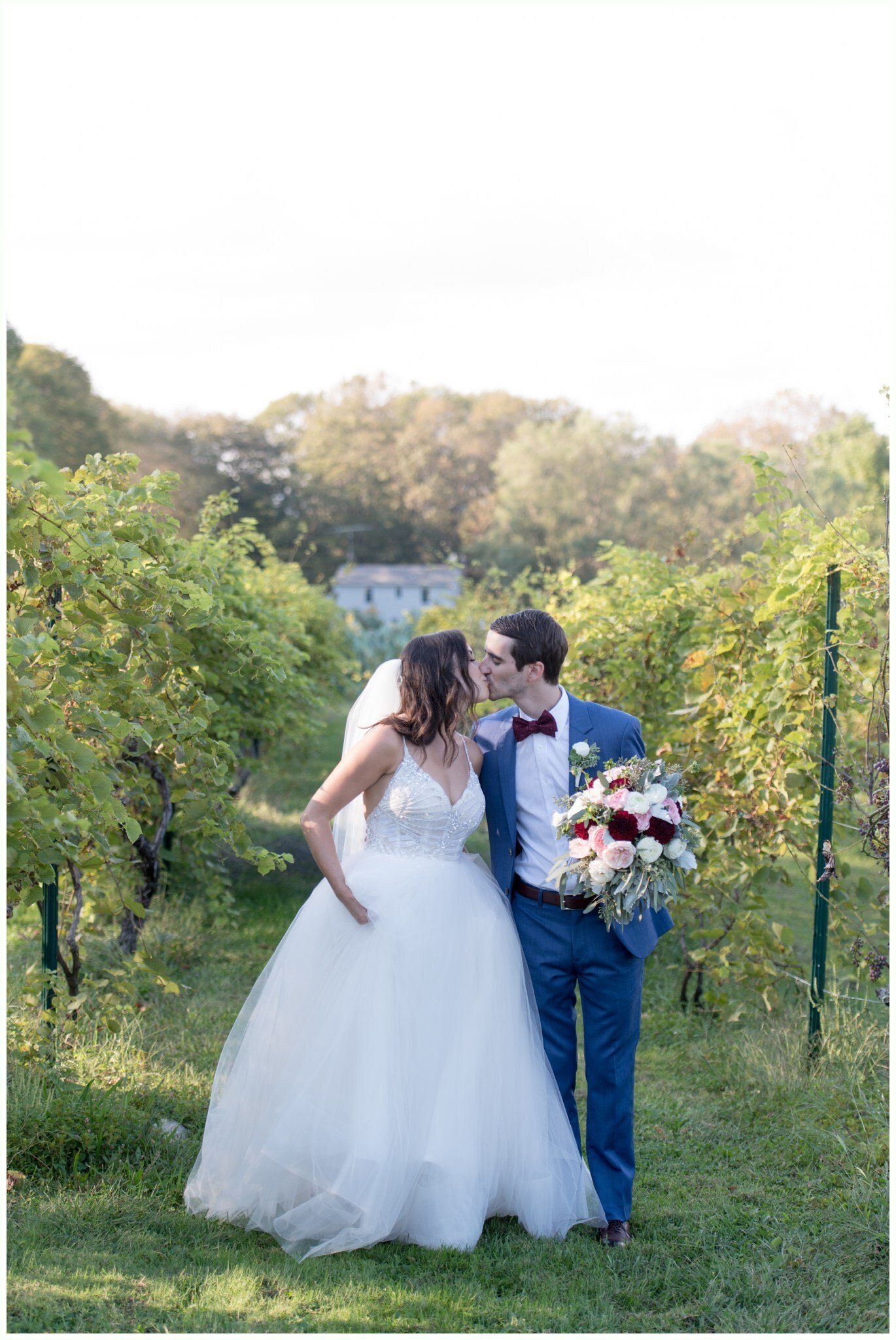 Bride and groom walking hand in hand in a garden, the bride holding a bouquet in a white gown and the groom in a blue suit
