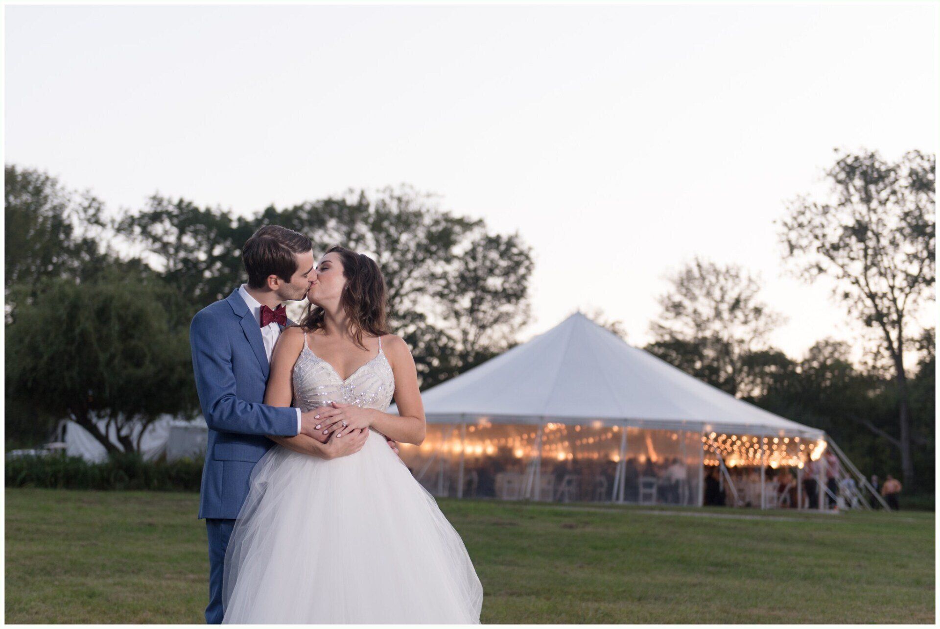Couple embracing outdoors at dusk near a lit white tent in a grassy field