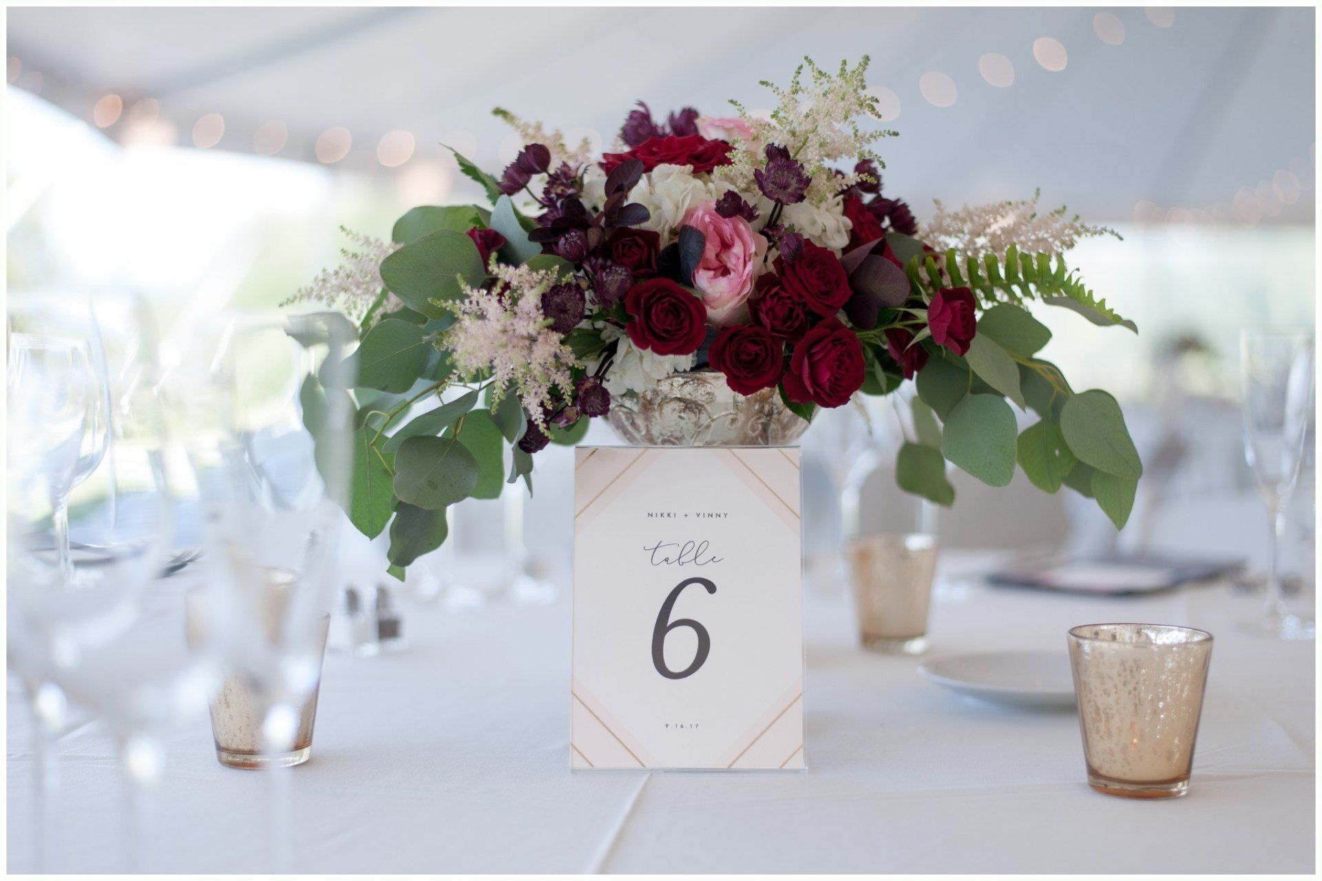 Floral centerpiece with burgundy and white flowers on a table marked with number 6 in a bright wedding reception