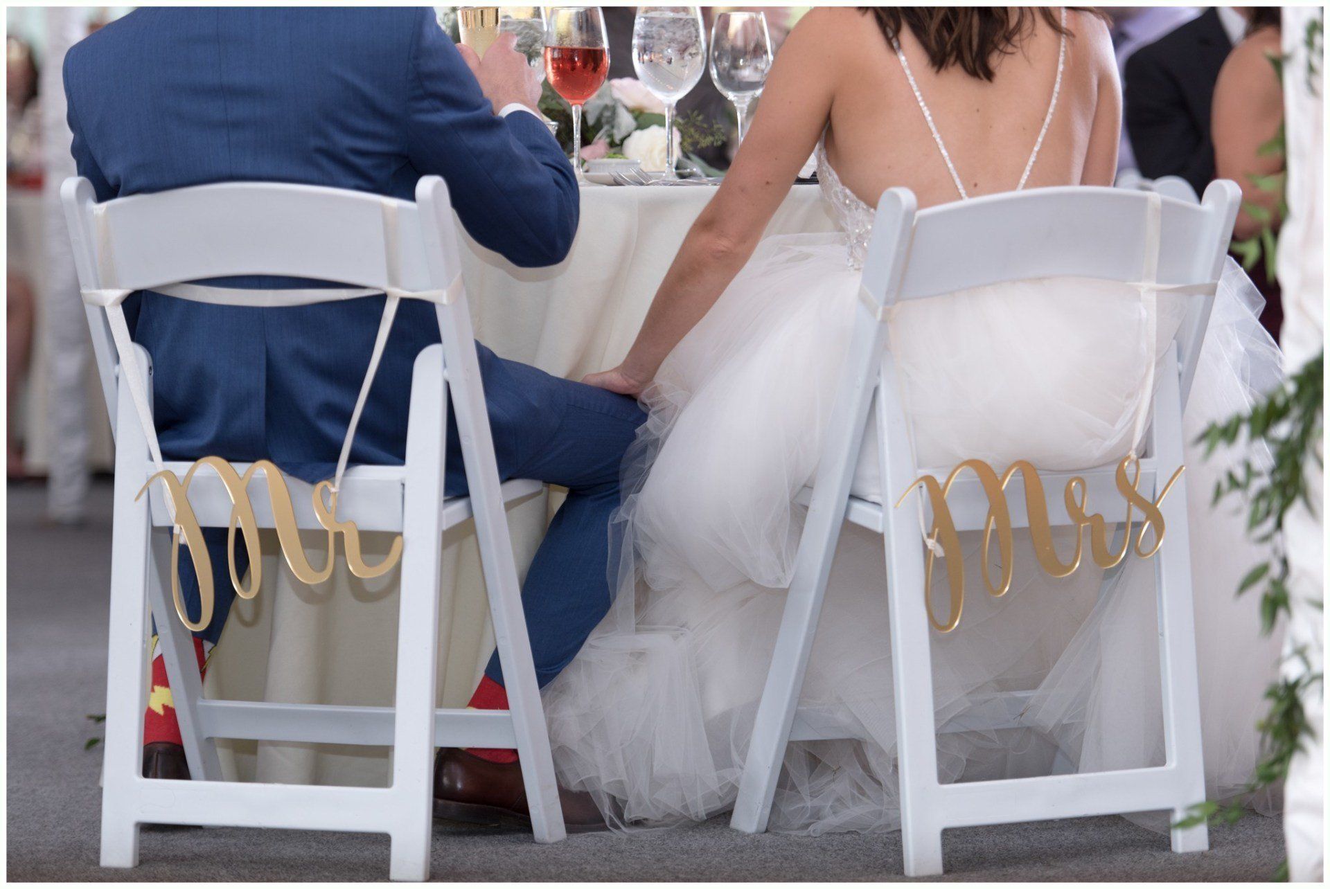 Bride and groom seated at a white-clothed outdoor wedding table, seen from behind