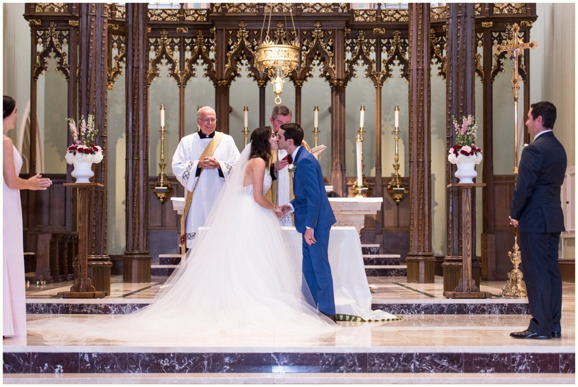 Wedding couple kissing at the altar in a church, with a priest and two guests nearby