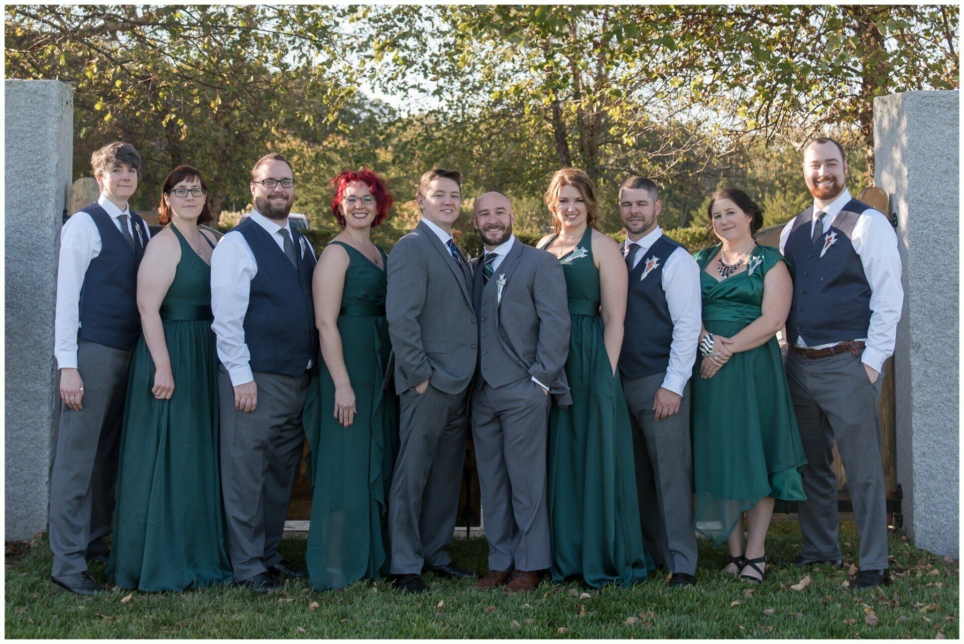 Group of people in formal attire standing outdoors in front of trees, posing together for a photo.