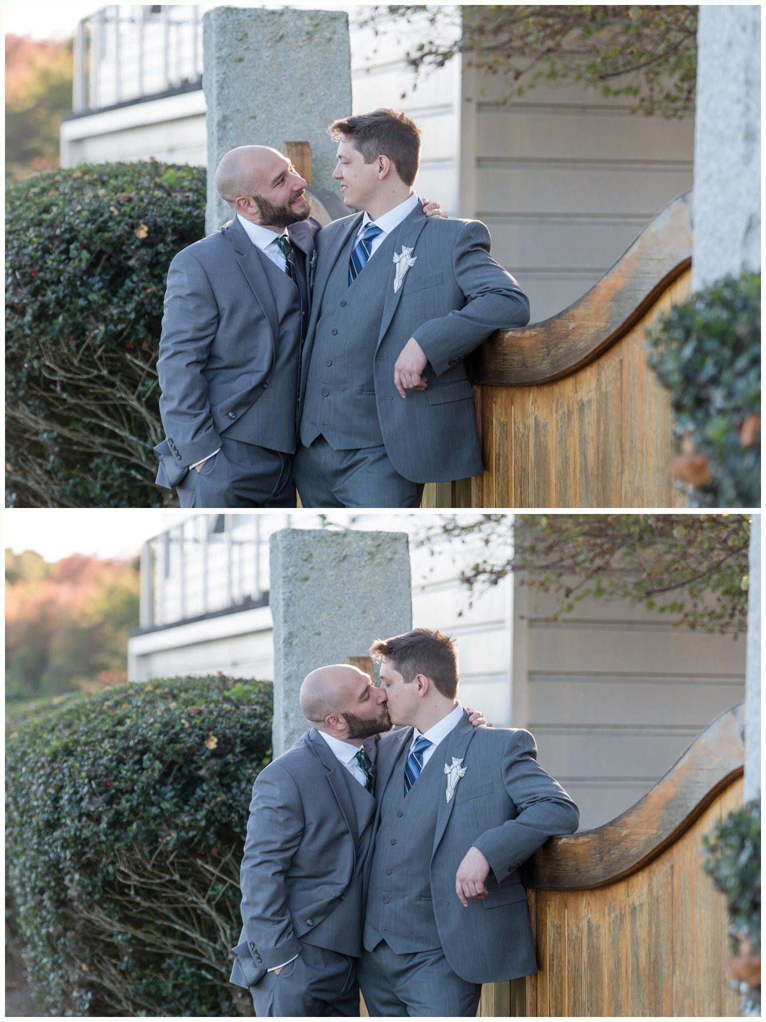 Two men in gray suits share a kiss beside a wooden fence and house exterior.
