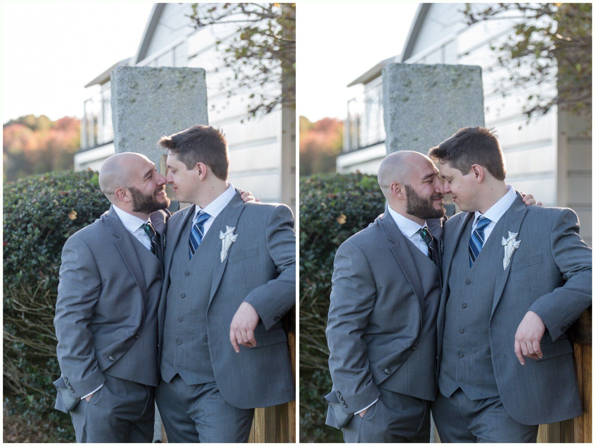 Two men in gray suits lean forehead to forehead outdoors beside a stone monument at sunset