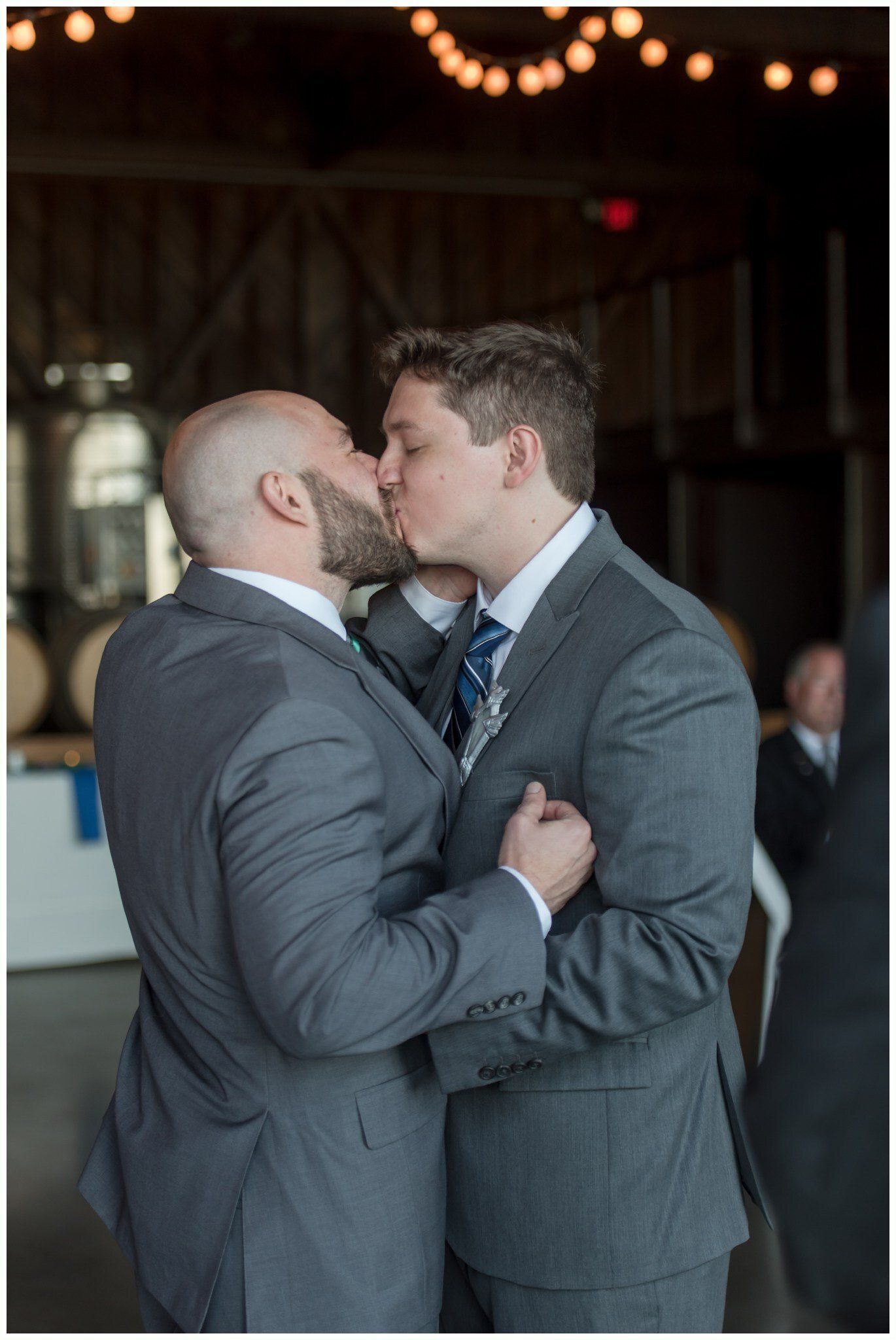 Two men in suits embracing and kissing at a dimly lit indoor event