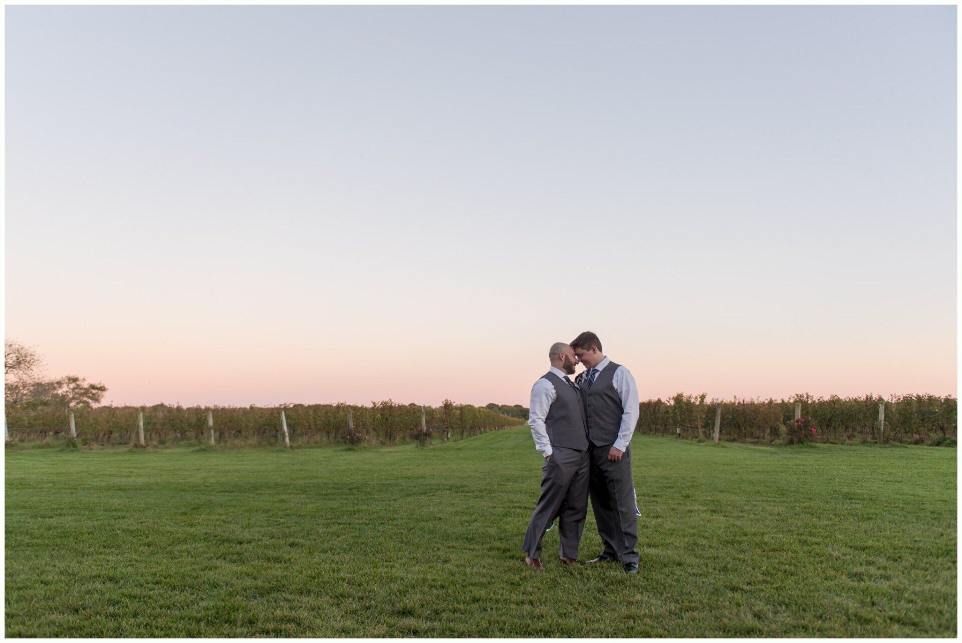 Two people standing close together in a grassy field at sunset