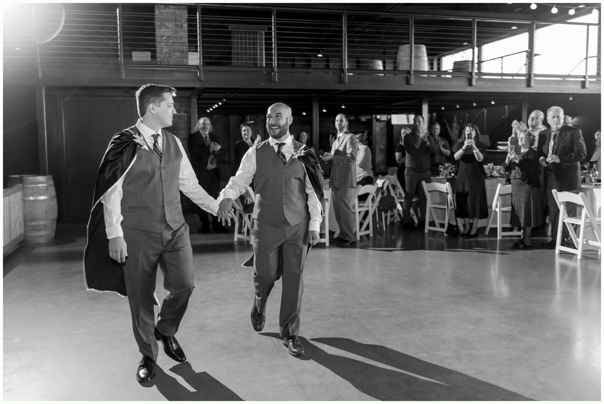 Two men in vests dancing in a hall while seated guests watch in the background