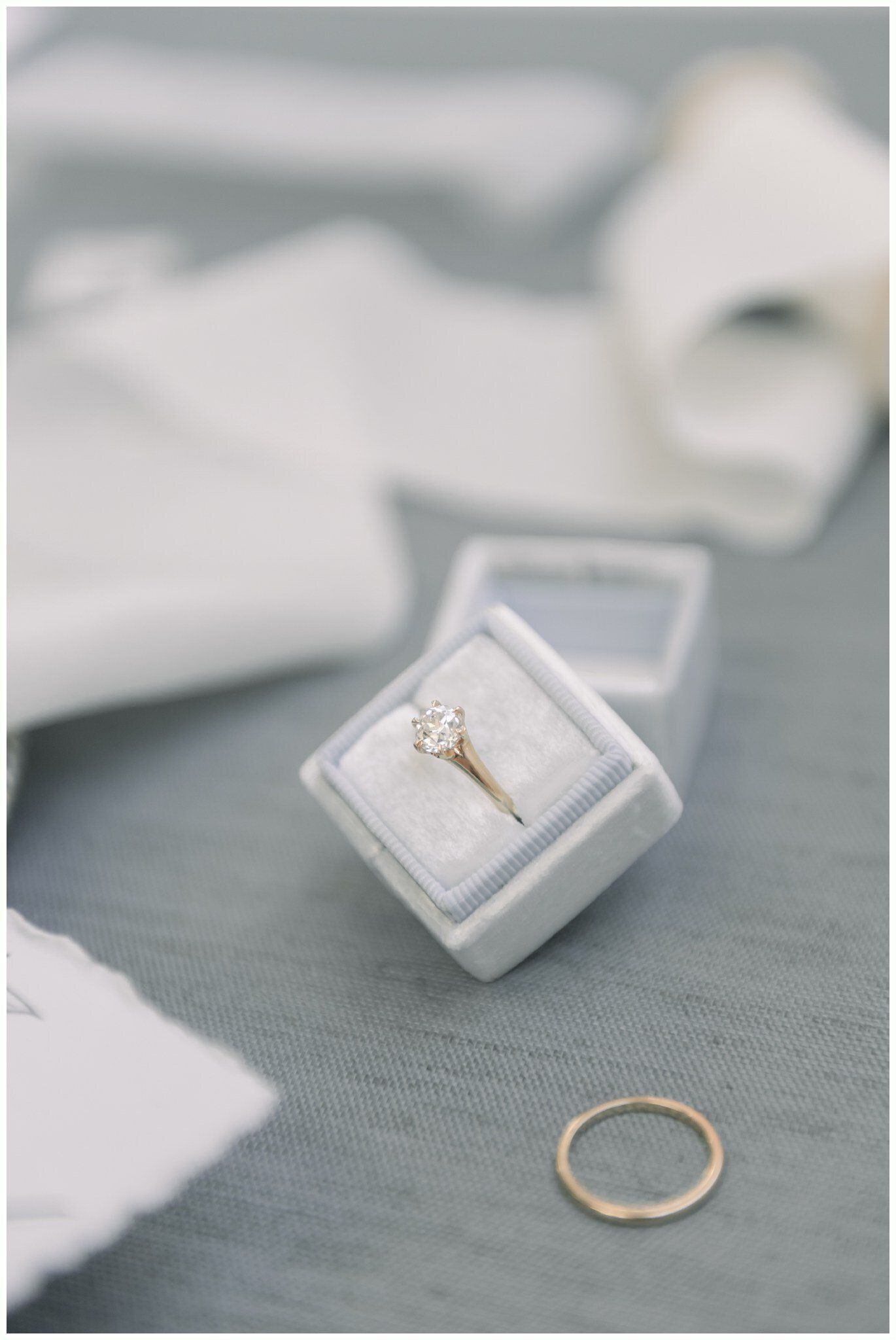 Engagement ring in a white velvet box with a gold band on a gray surface