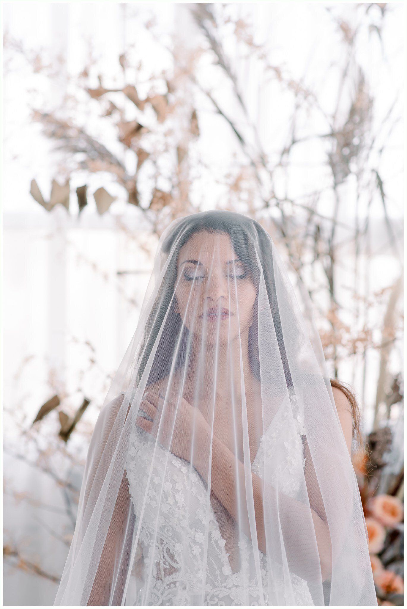 Bride in a white veil standing before a soft floral backdrop