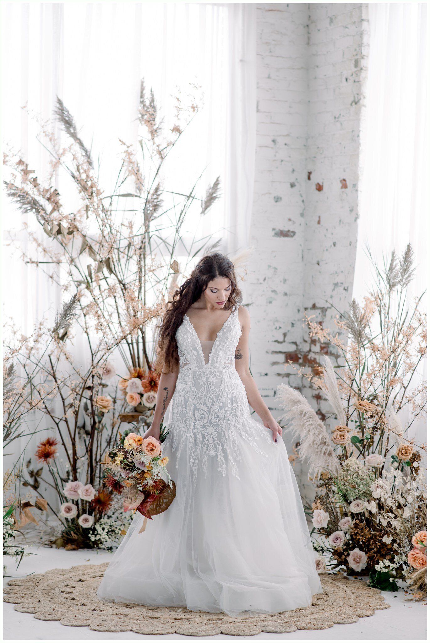 Bride in a white lace gown standing among floral arrangements before a white column backdrop