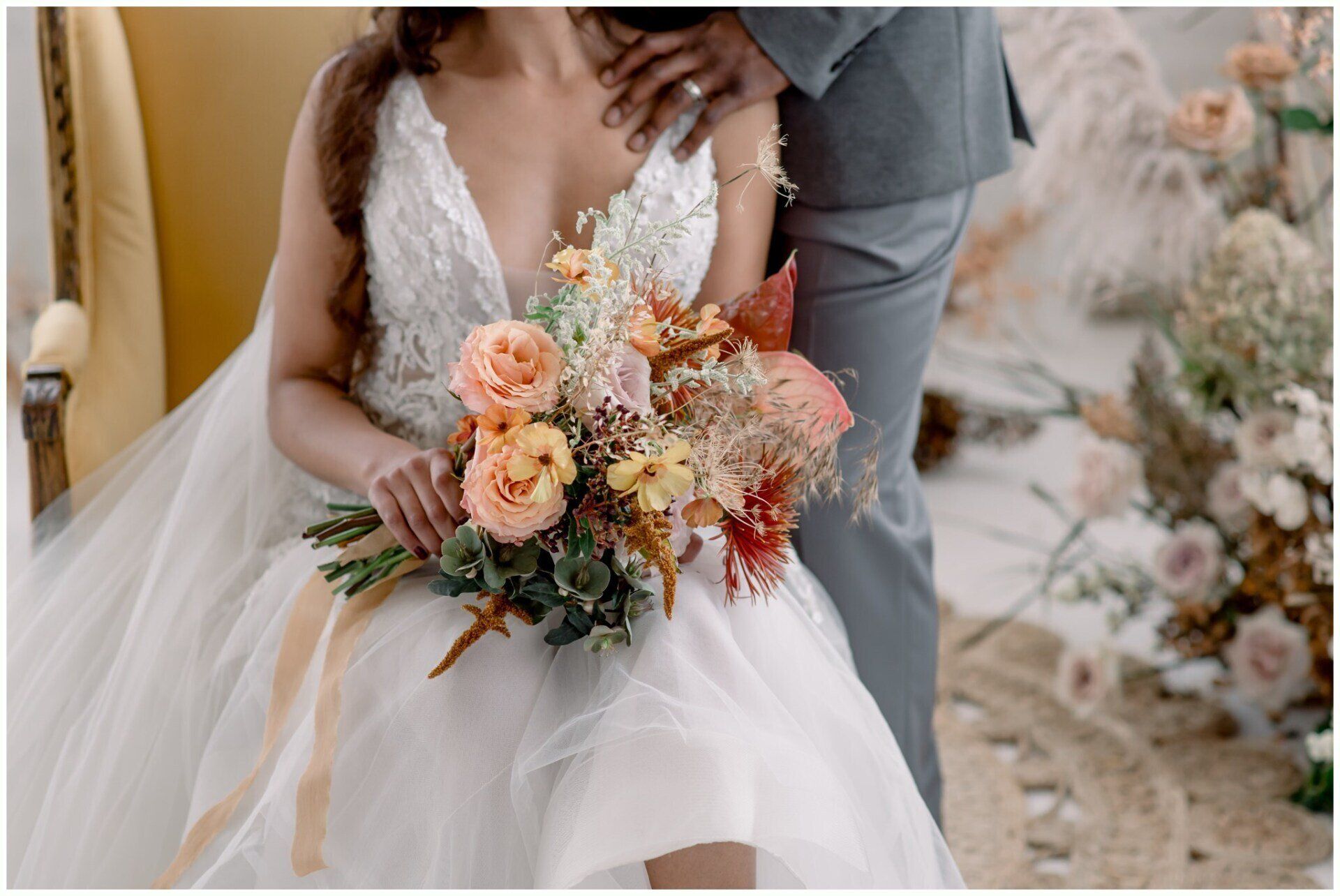 Bride and groom seated with pastel wedding bouquet and veil in a soft, romantic setting