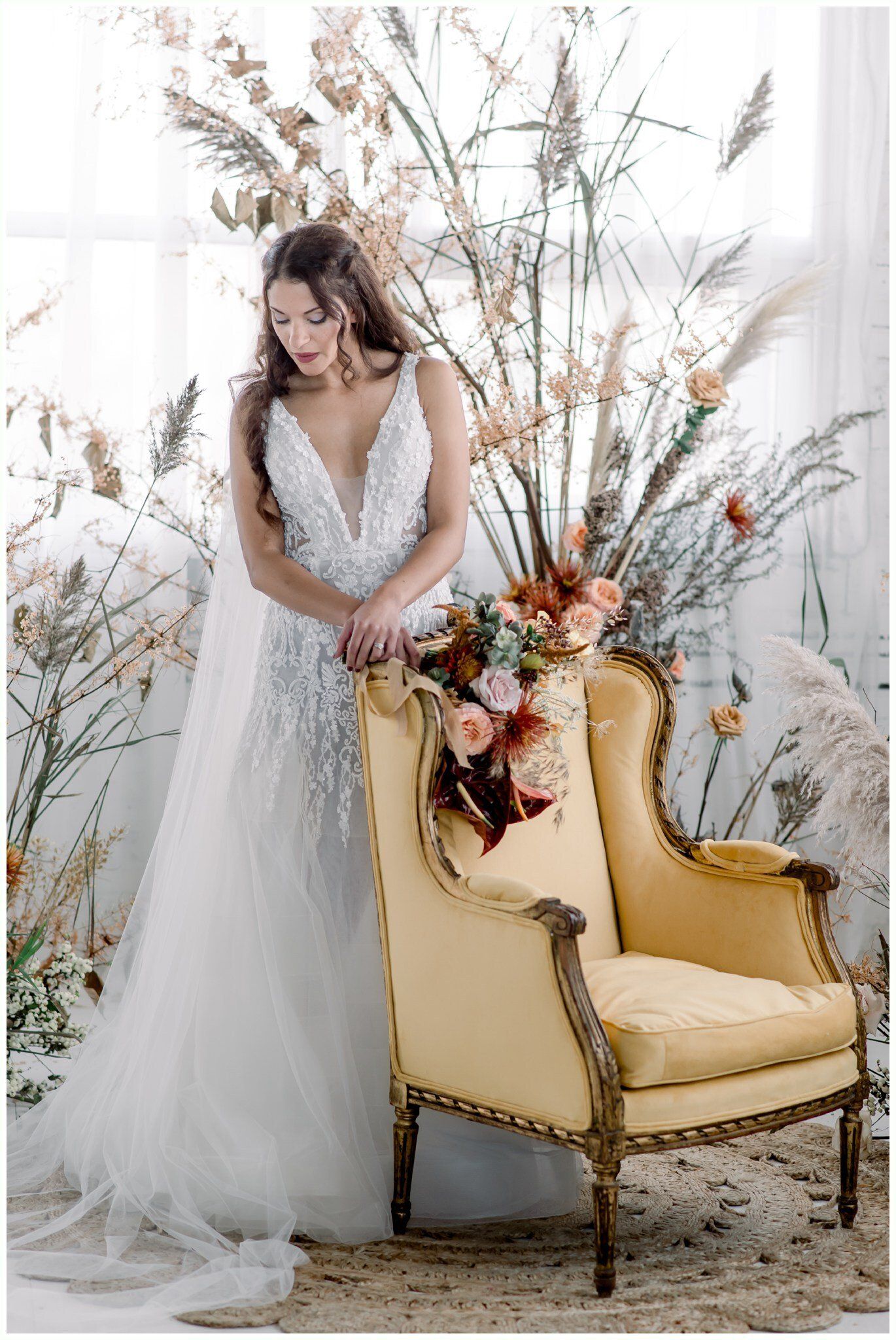 Woman in a white dress beside a cream armchair with floral arrangements in a bright, elegant room