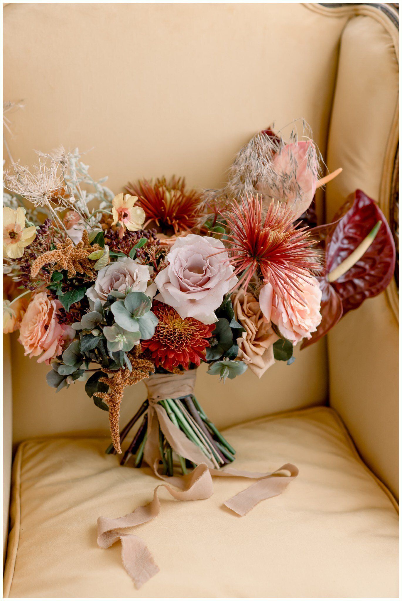 A pastel floral bouquet with pink and white flowers resting on a cream leather chair