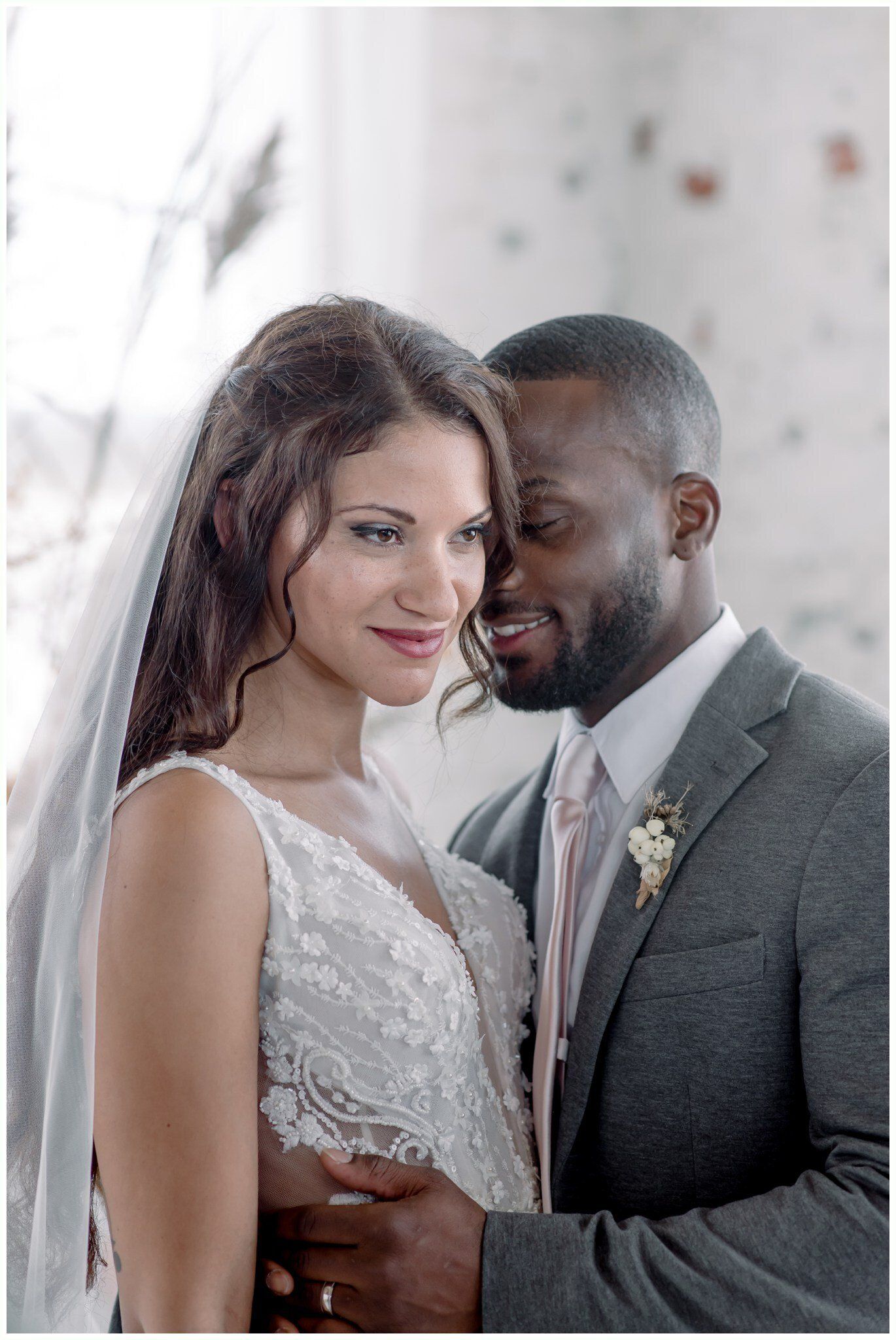 Couple embracing softly in wedding attire by a bright window