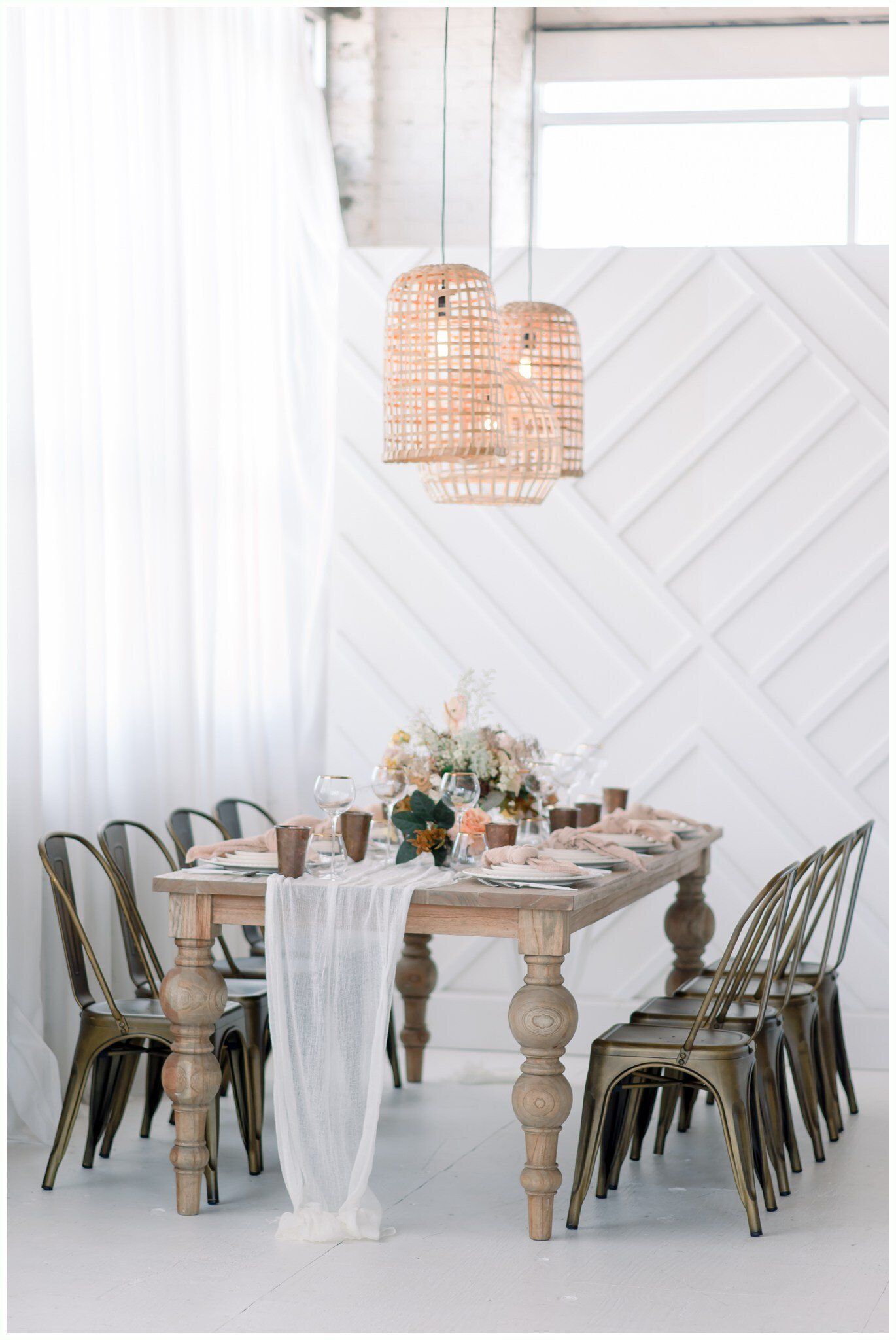 Elegant dining room with a rustic table, mixed chairs, and woven pendant lights in a bright white interior