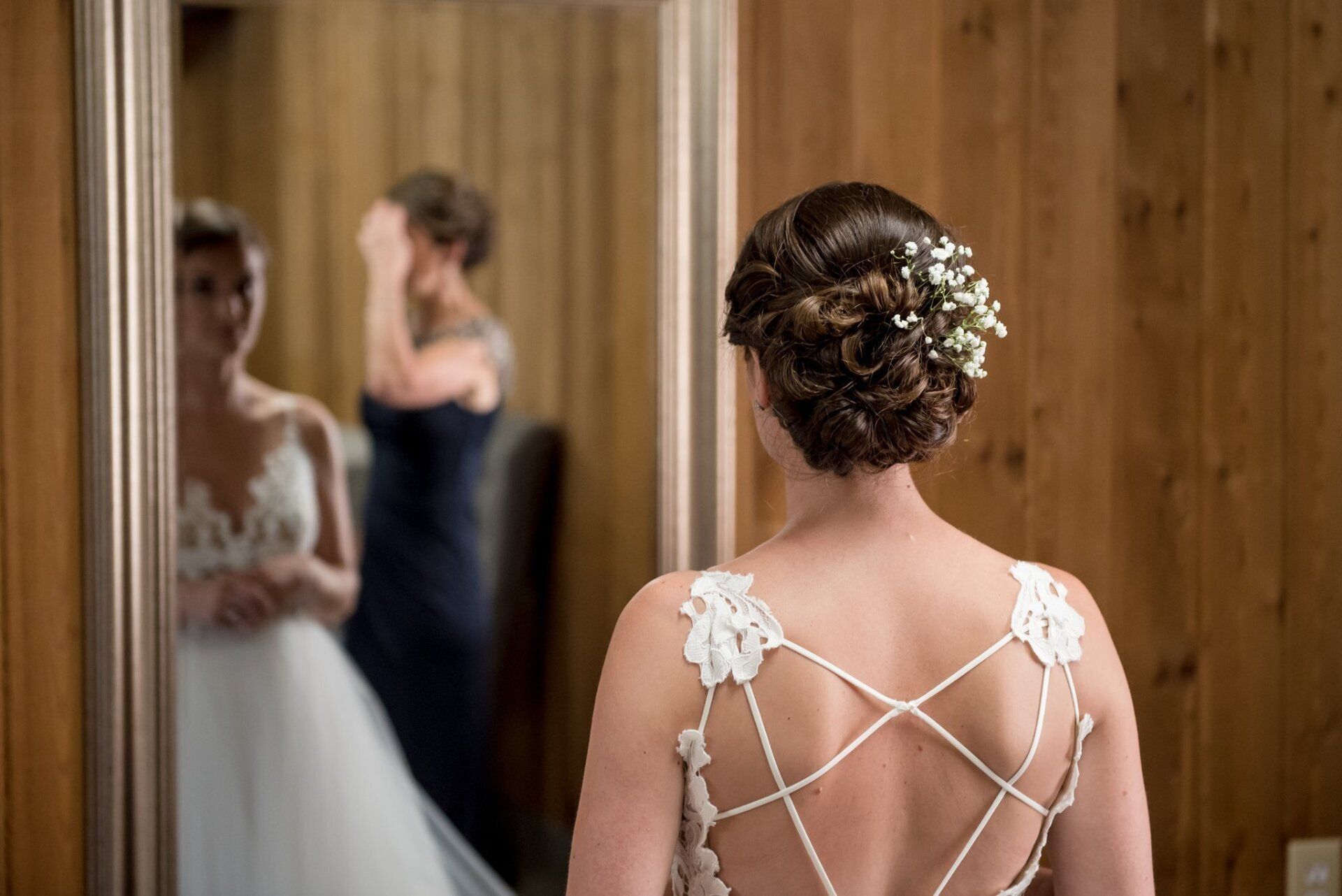 Bride seen from behind admiring her reflection in a mirror, wearing a lace wedding dress in a bridal room