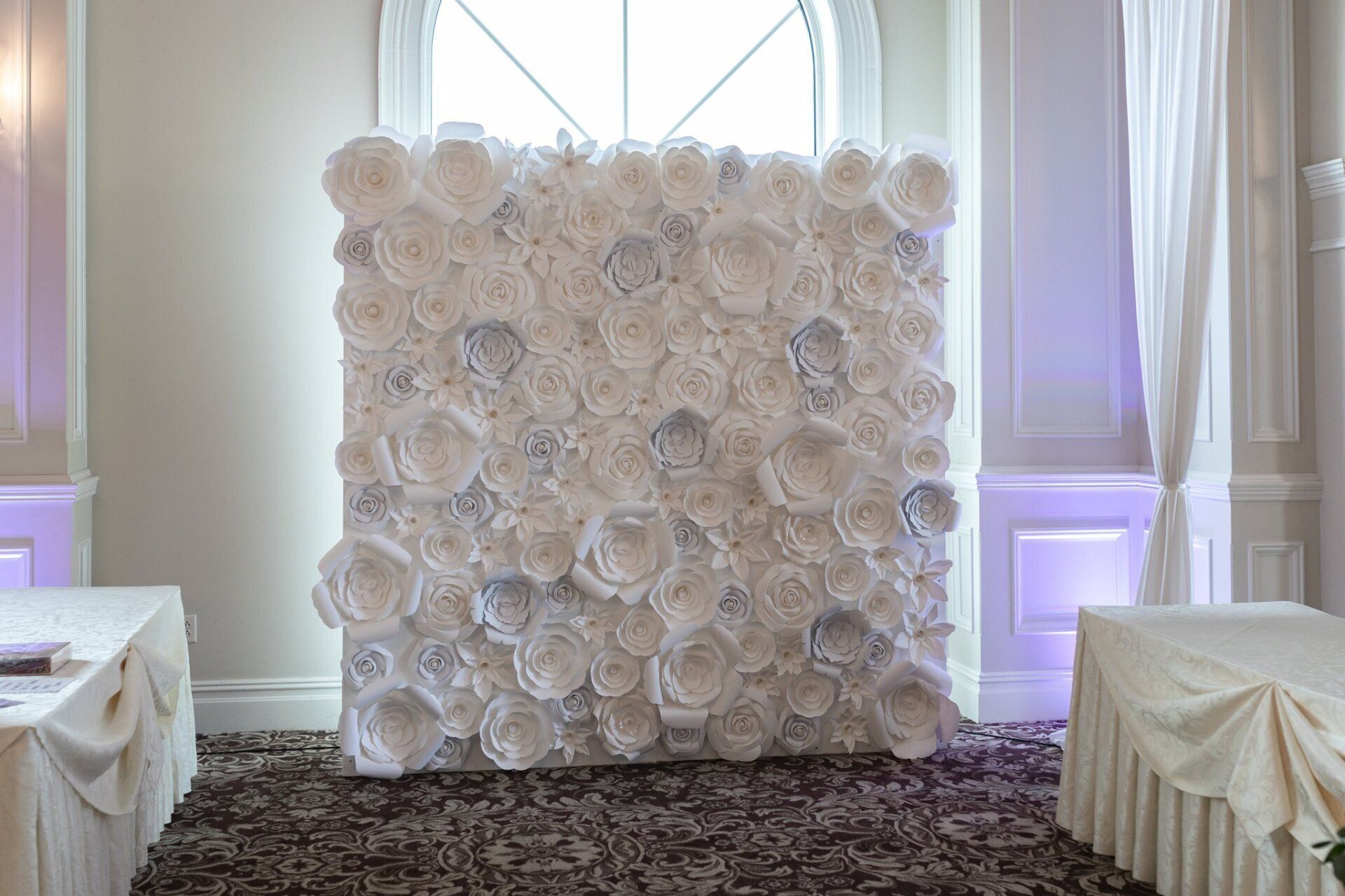 Wall of white paper flowers against tall windows in a bright room