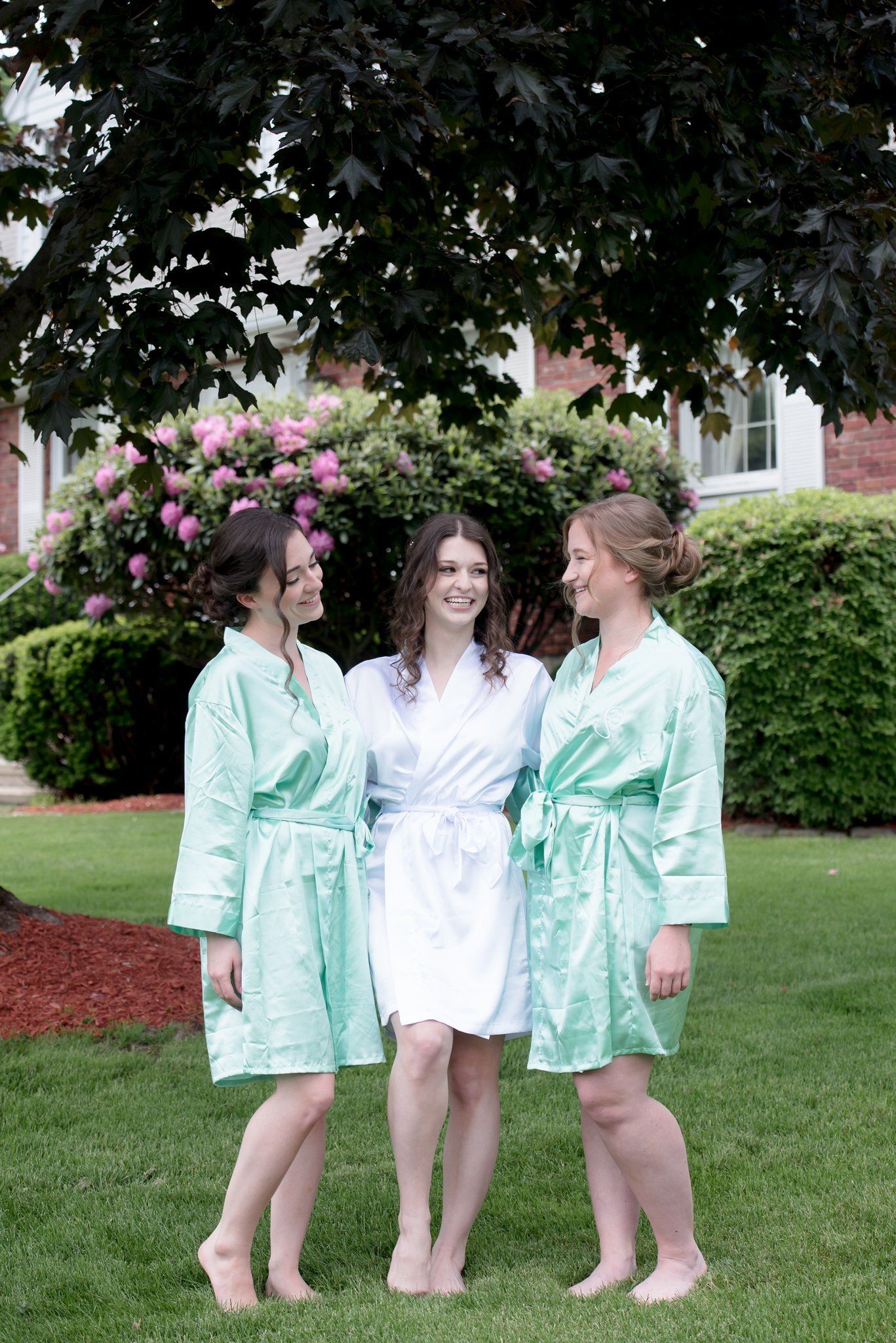 Three people in mint robes standing together outdoors in front of a house